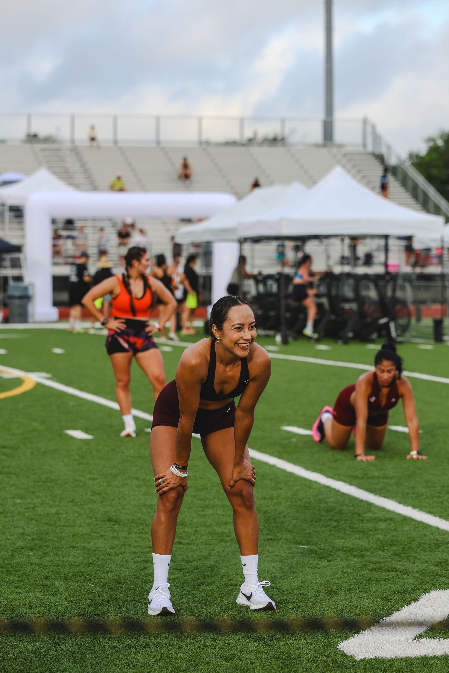 Female athletes stretching and warming up on a green turf field at an outdoor track and field competition.