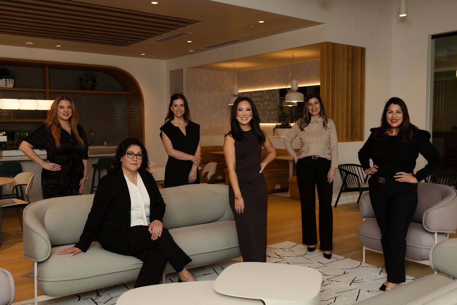 Professional business team poses confidently in a modern office lounge with gray couches and contemporary decor.