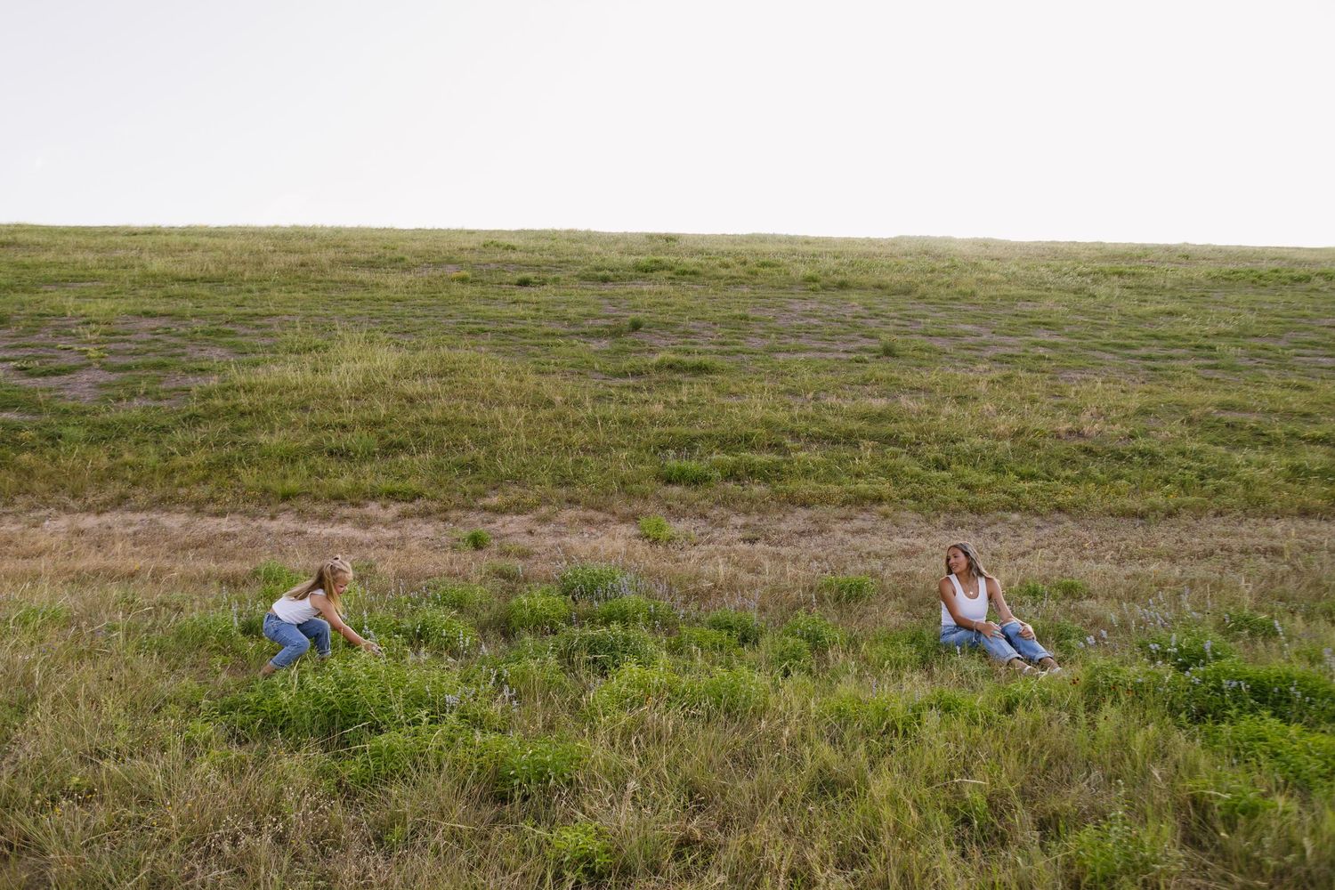 Two women sitting on a lush green grassy hillside on a cloudy day.