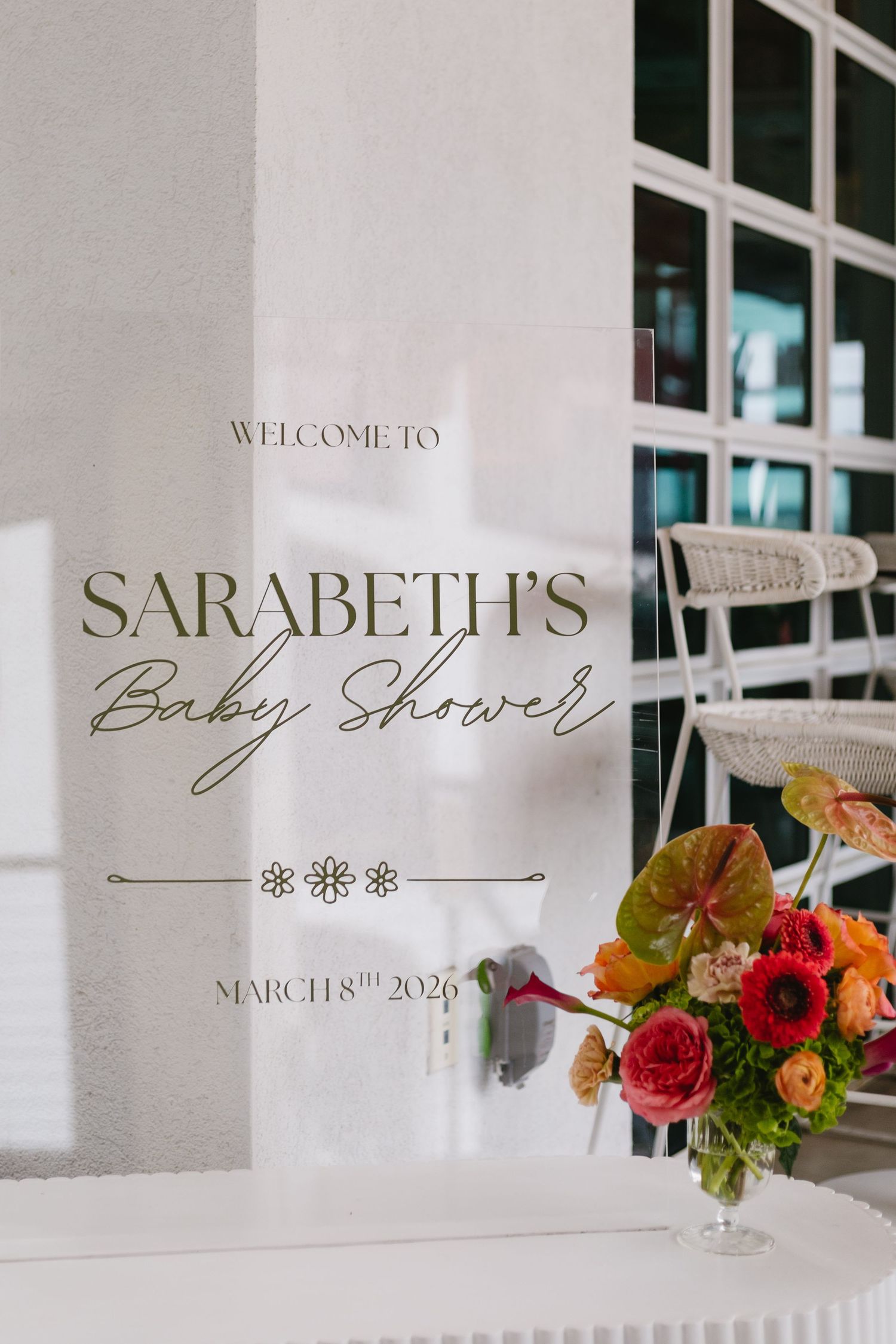 Elegant baby shower welcome sign for Sarabeth on March 8th, 2026, with colorful floral arrangement.