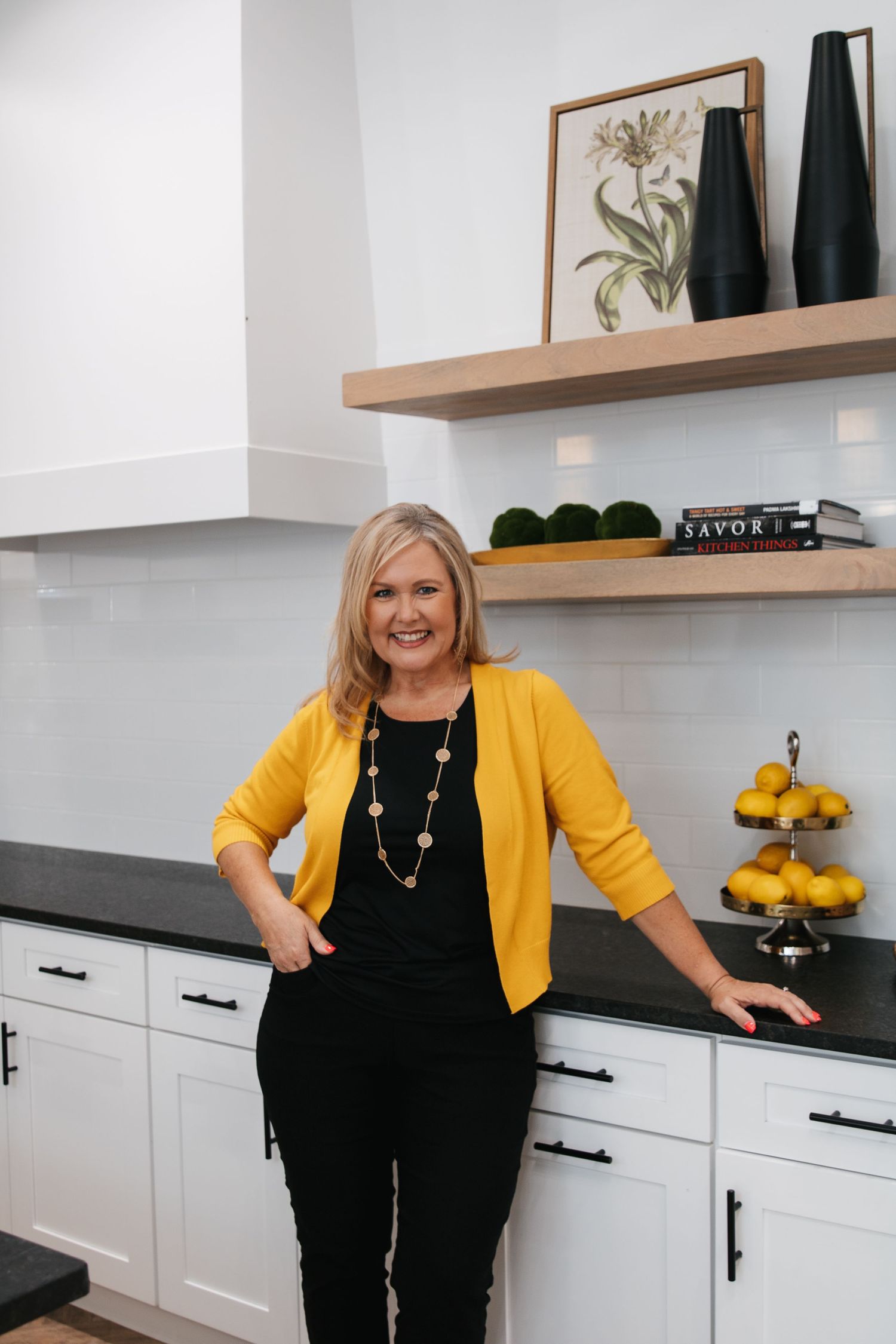 Professional wearing a yellow cardigan and black outfit poses in a modern white kitchen with lemons on the counter.