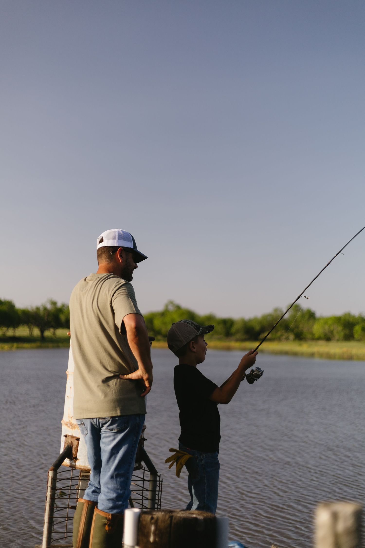 Two people standing on a wooden dock fishing together on a calm lake during a summer day.