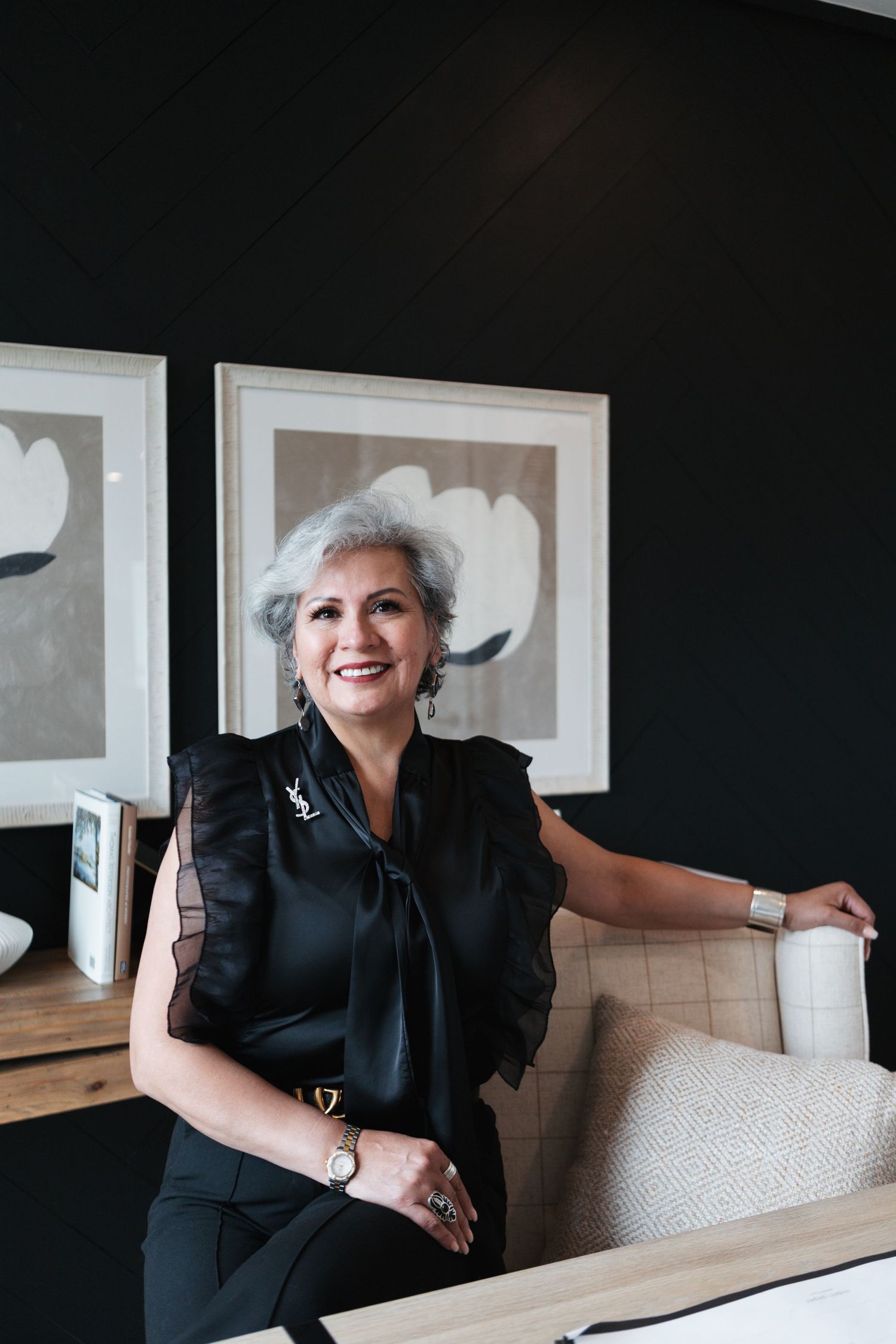 A woman in a black outfit sits on a beige couch in different playful poses.