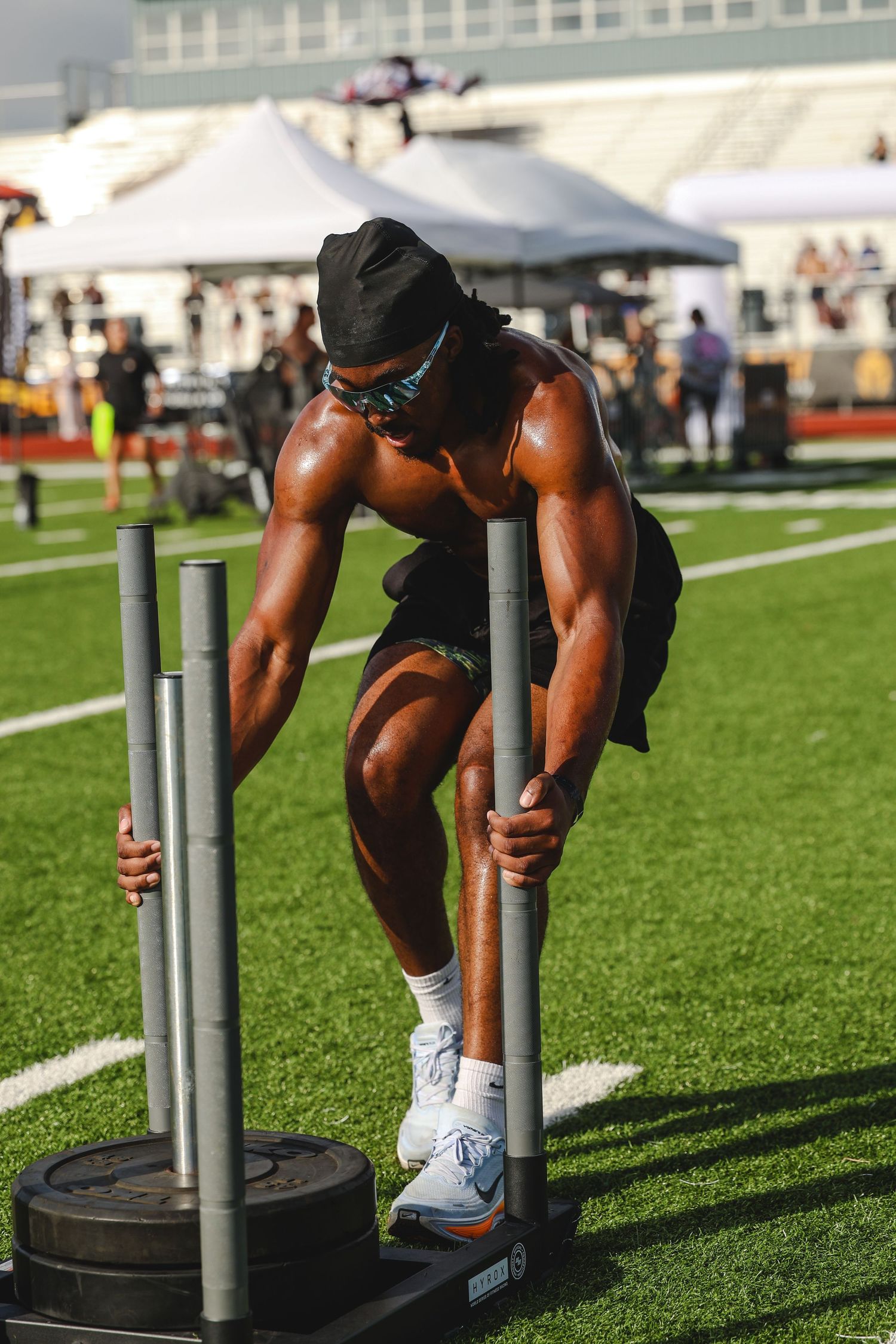 Muscular athlete pushes weighted sled on green turf during outdoor fitness competition.