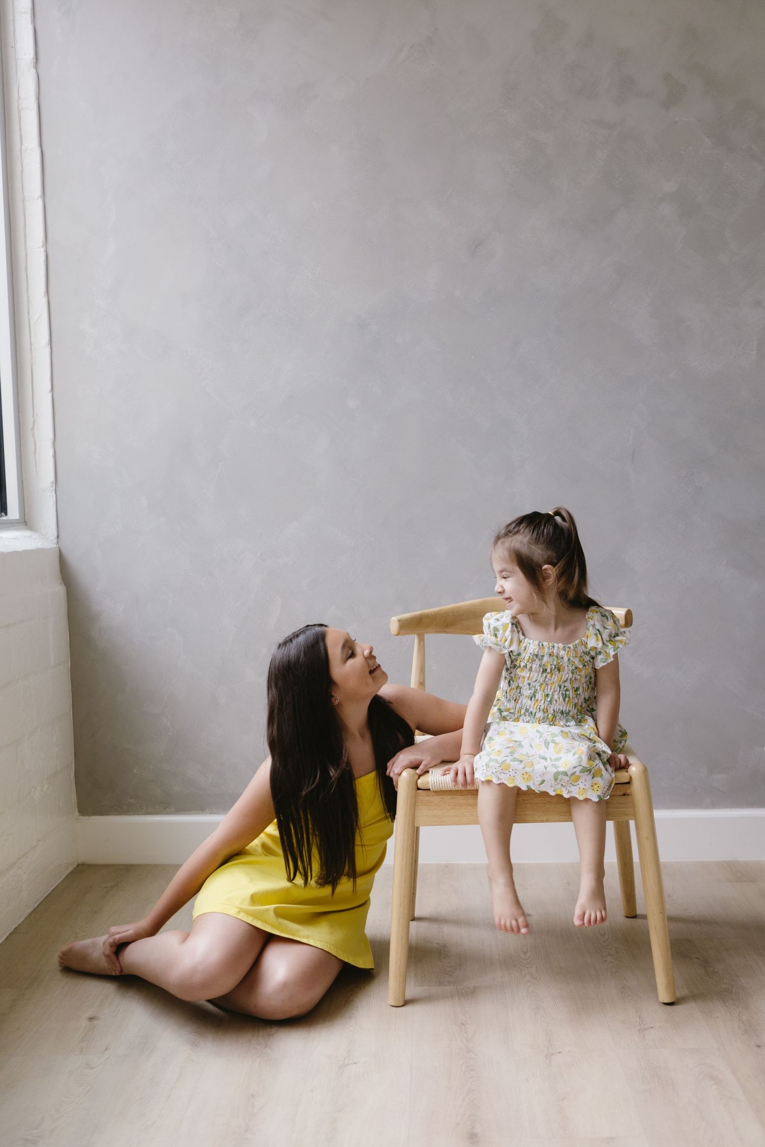 A tender moment between two people by a wooden chair in a minimalist setting.