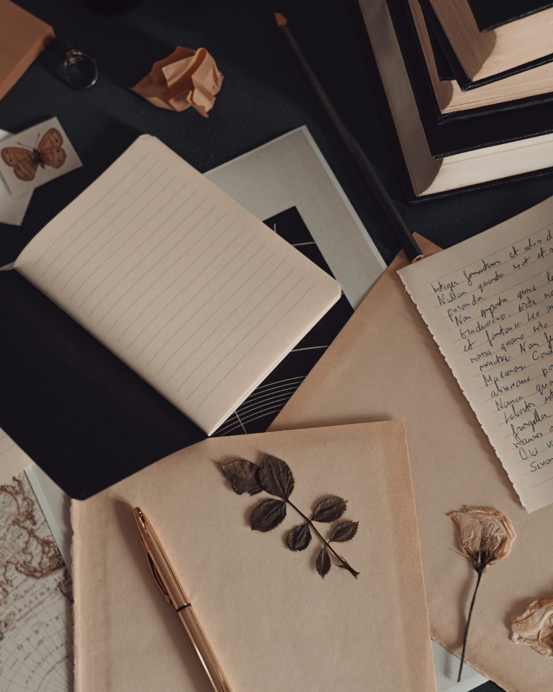 Open notebooks with handwritten text and dried flowers arranged on a dark surface.