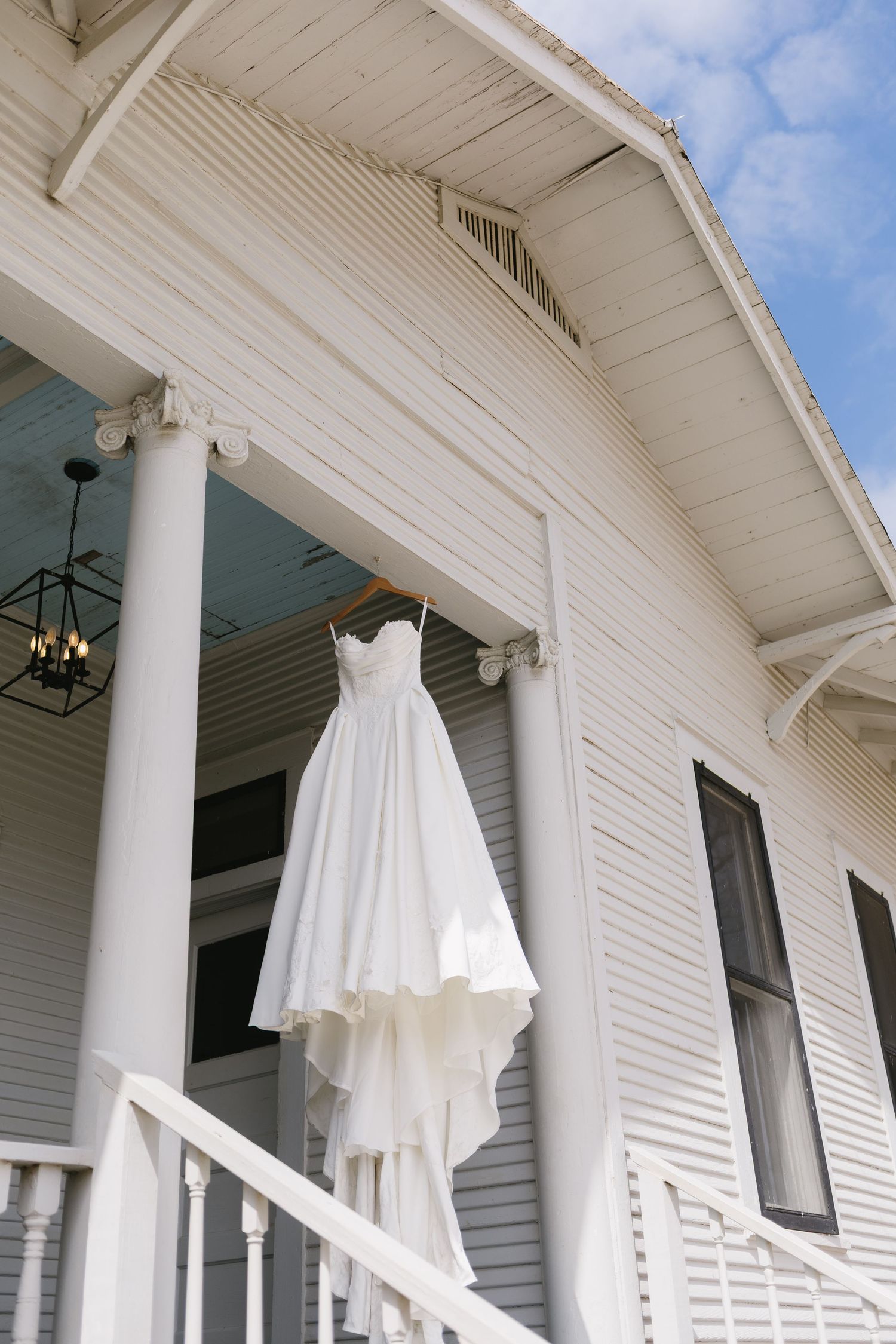 White wedding dress hanging on porch of charming white wooden church on a sunny day.