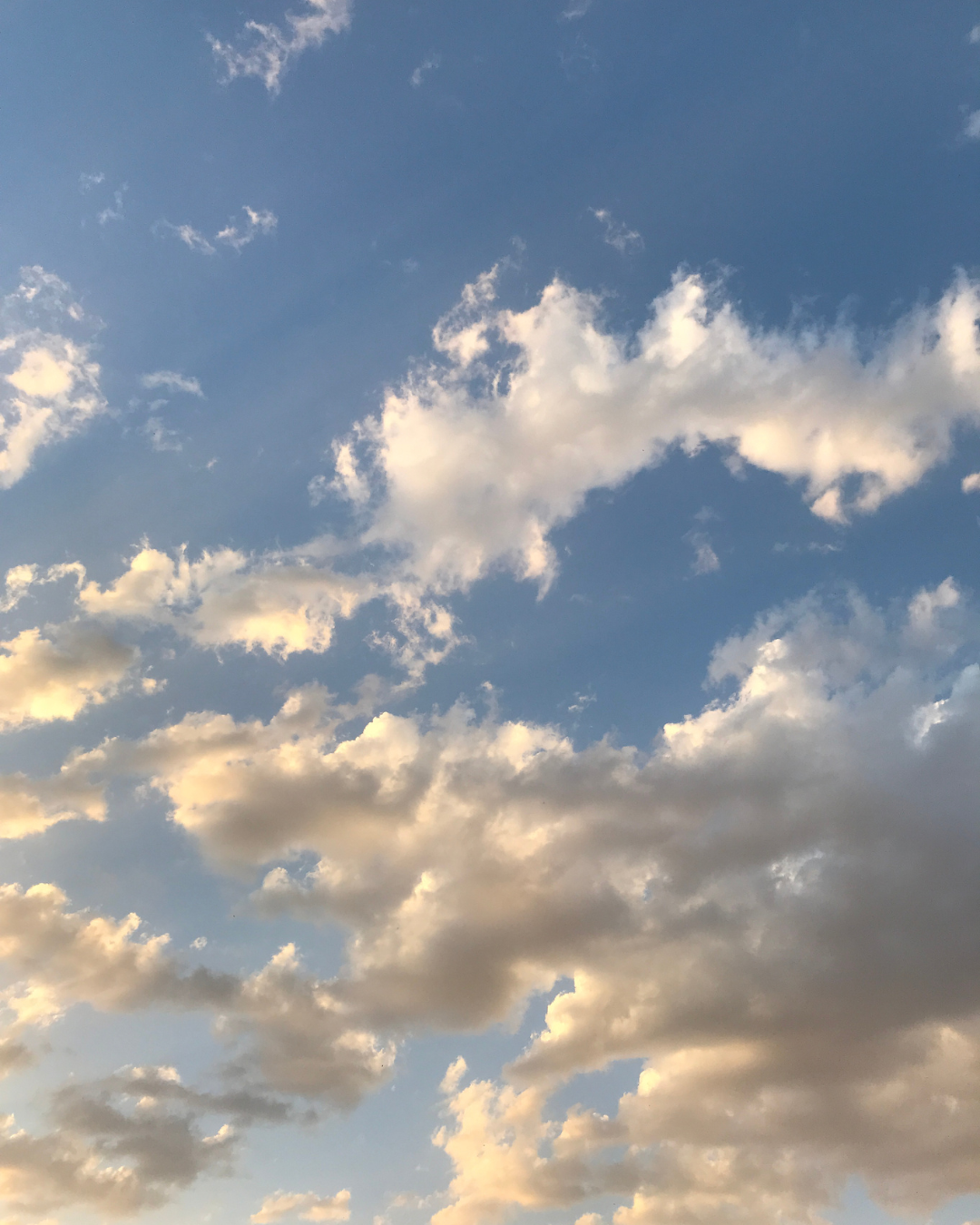 Dramatic sunset sky with fluffy white and golden clouds against bright blue background.
