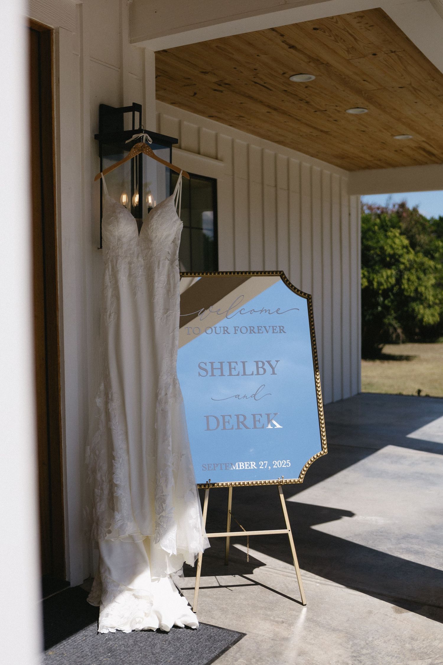 A wedding dress hangs next to a blue hexagonal sign with text displayed at an outdoor venue.