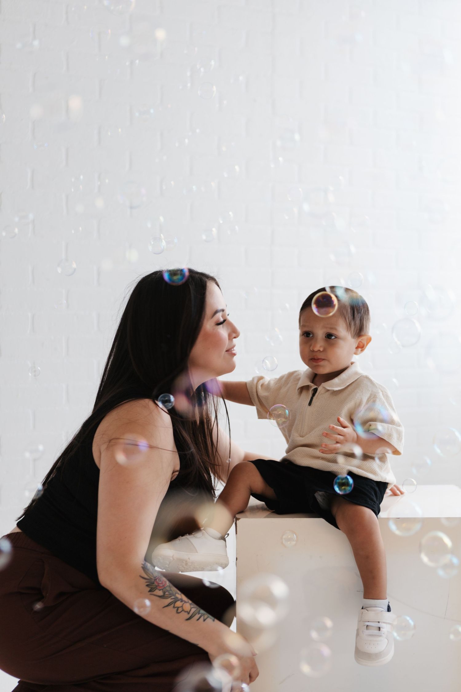 A loving parent embraces and plays with a cheerful baby while white bubbles float through the air.