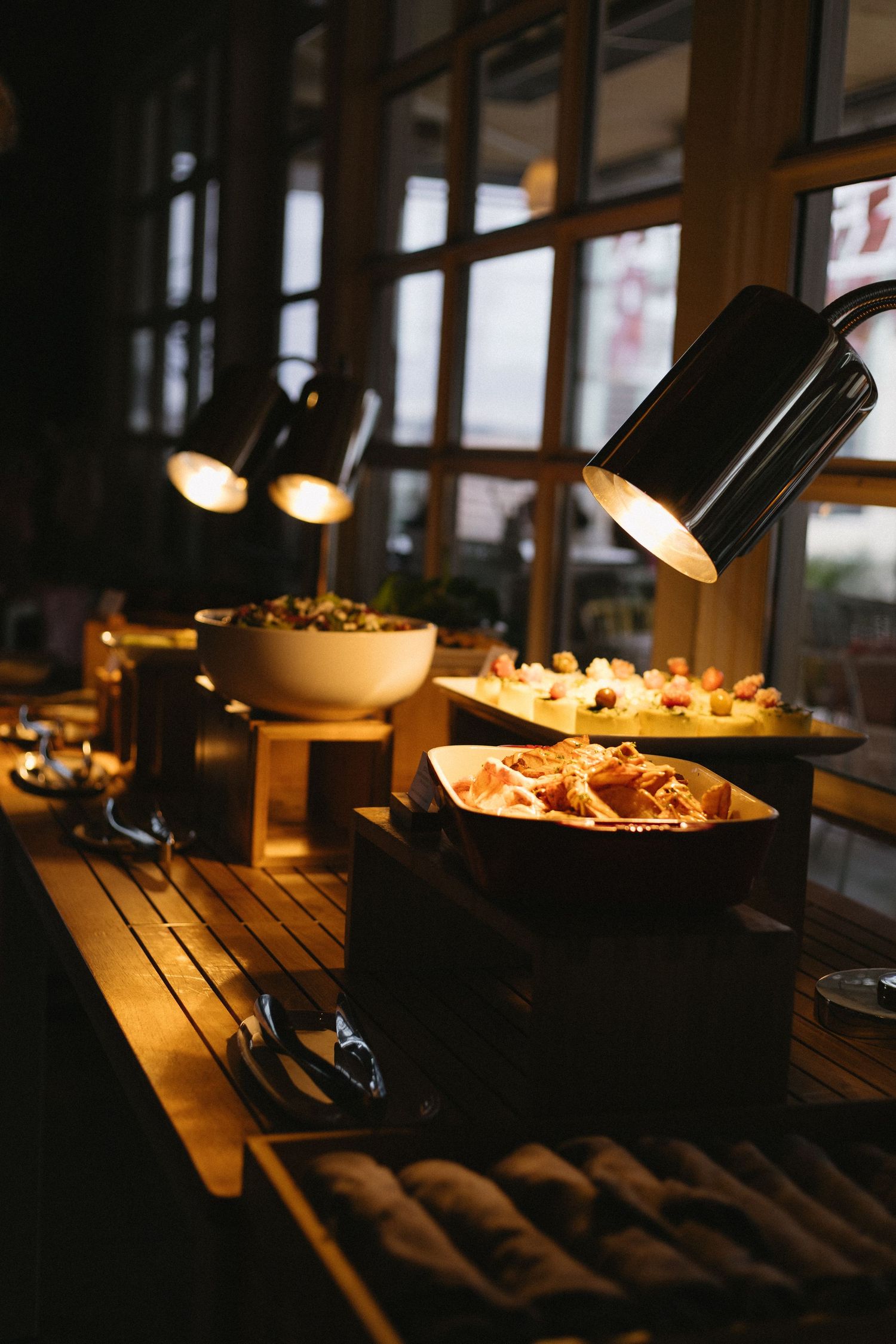 Warm buffet spread with heat lamps illuminating dishes on a wooden table in a dimly lit restaurant.
