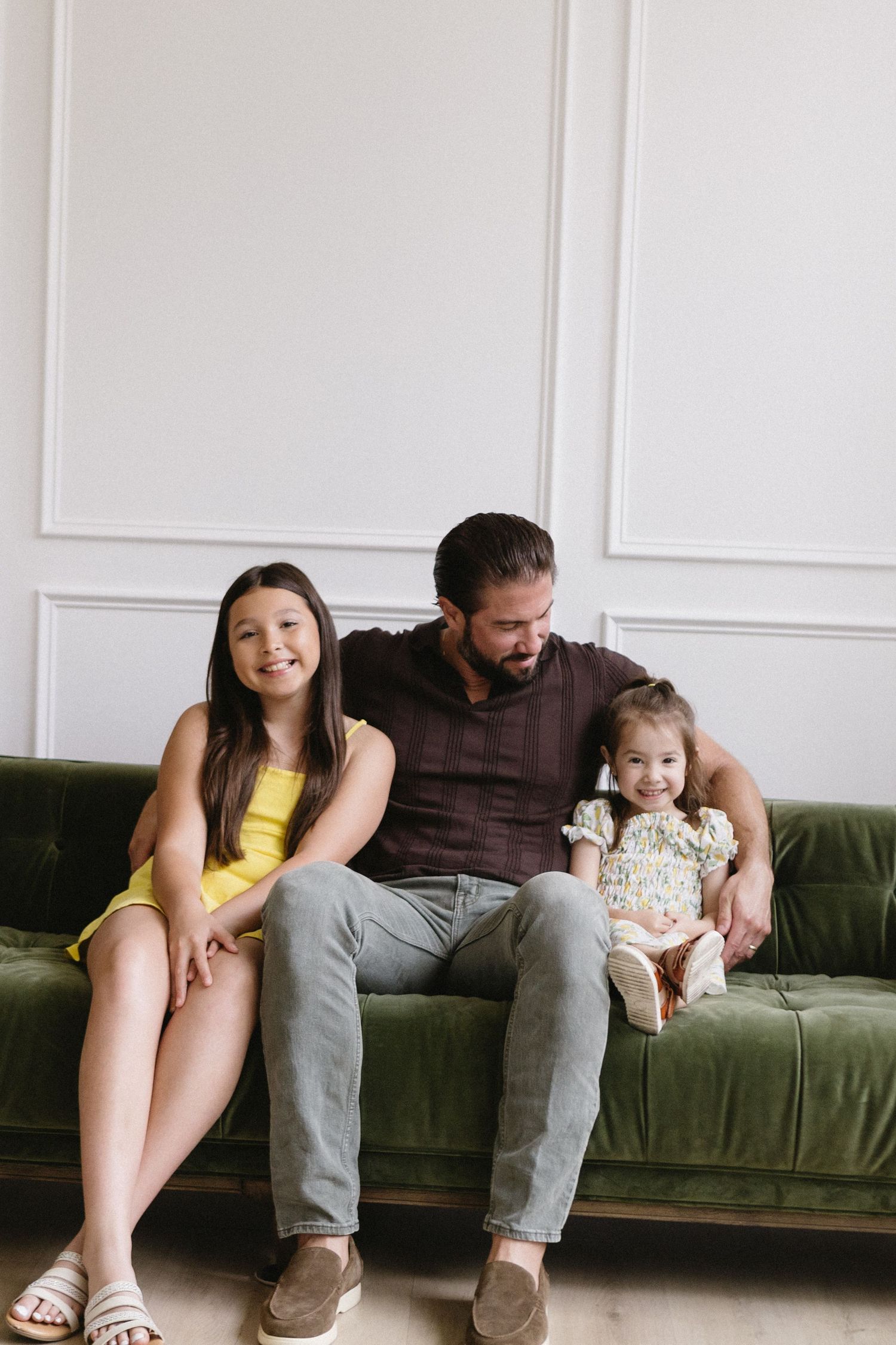 A casual family portrait on a green velvet sofa with white paneled walls in the background.