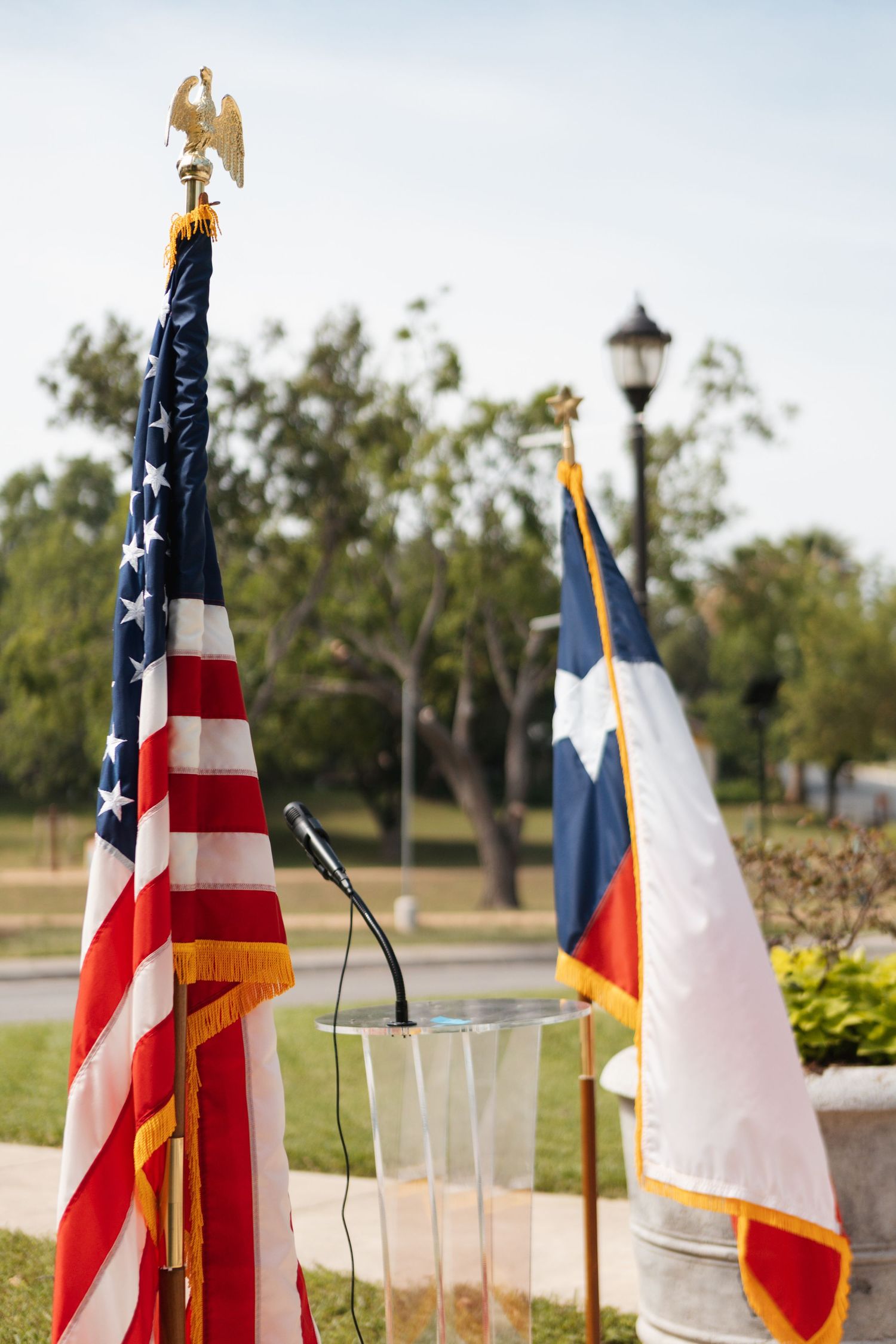 Outdoor podium with American and Texas state flags at a public ceremony in a park setting.