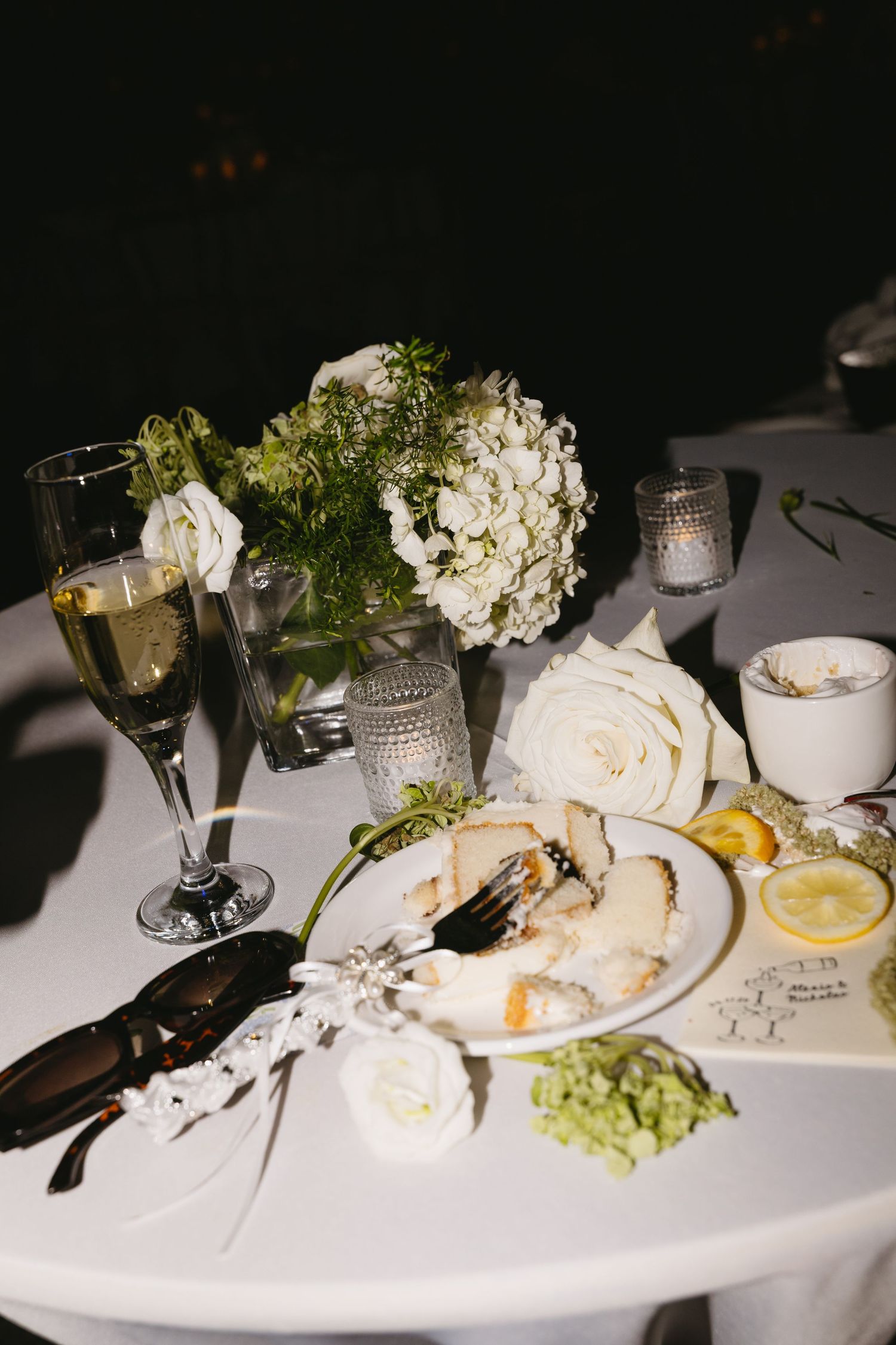 Elegant wedding reception table with white roses, hydrangeas, champagne glass, and a dinner plate with food.