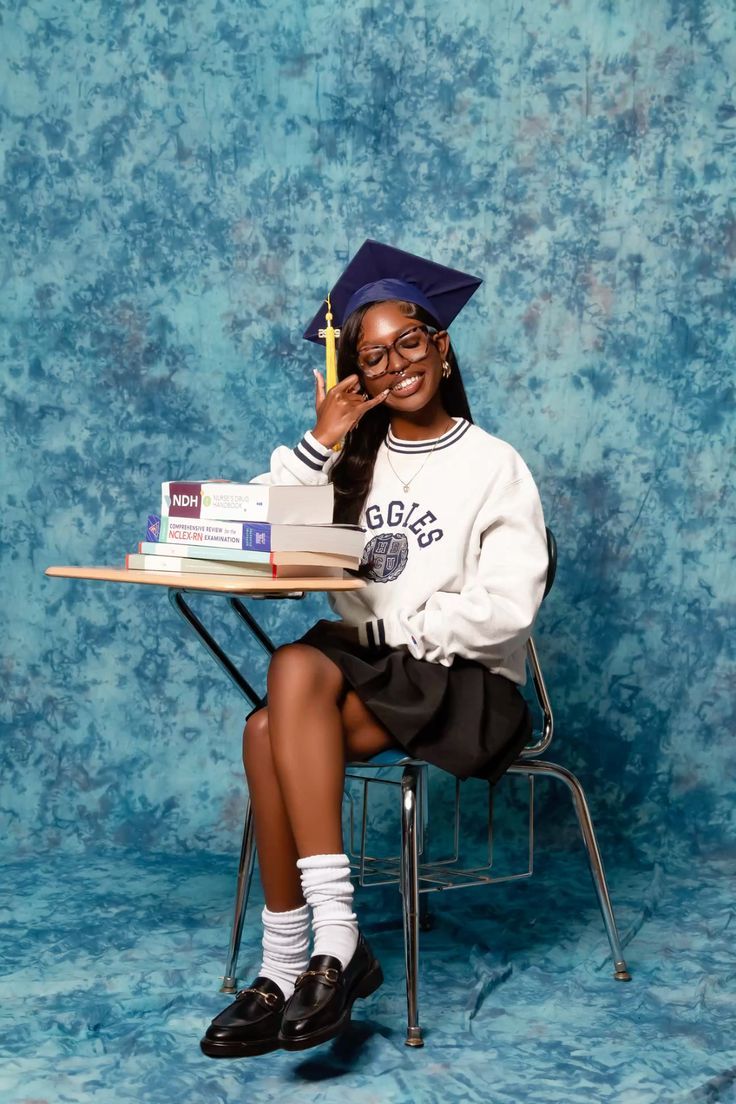 Graduate in cap and gown poses with books against blue backdrop for celebration photo.