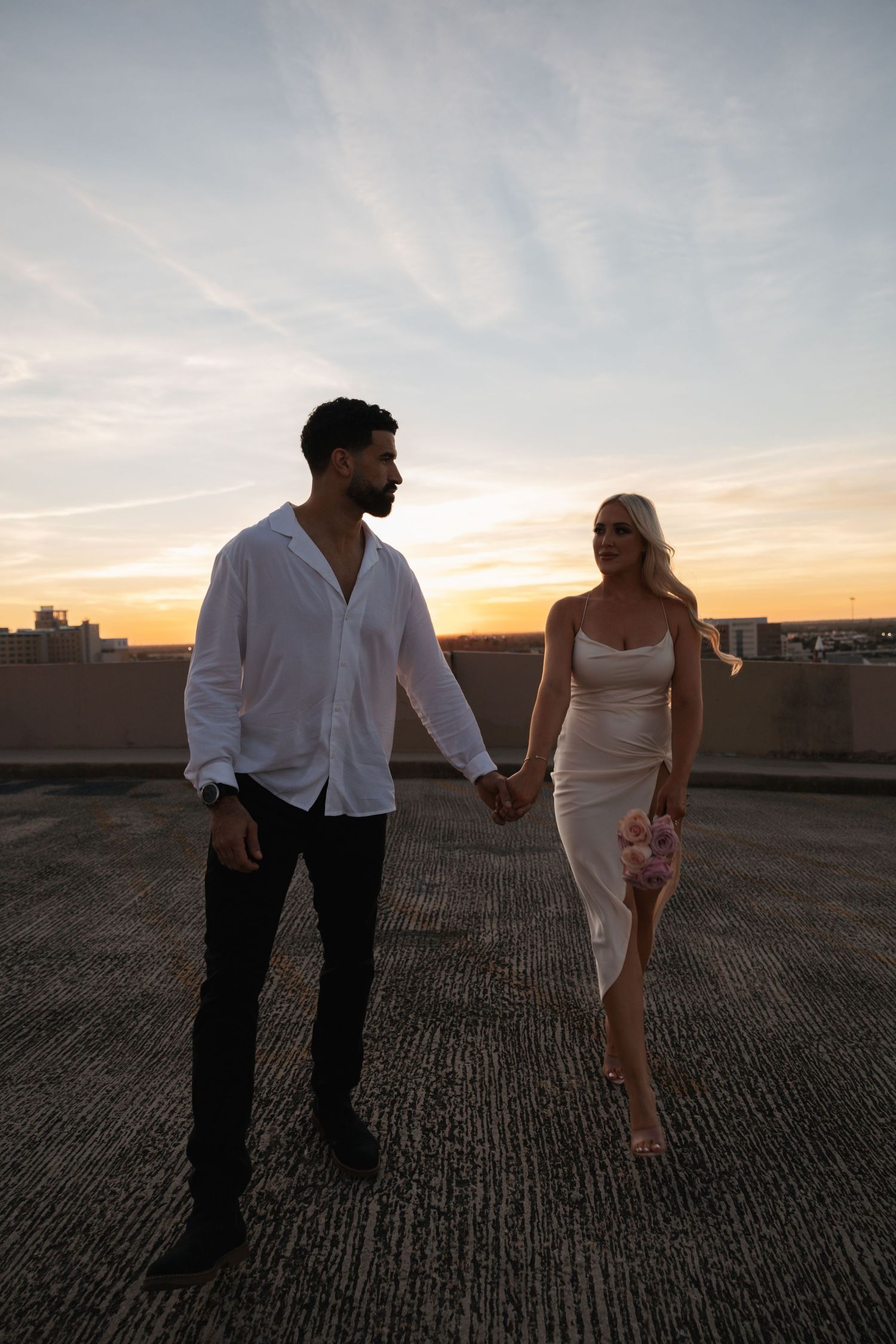 A couple walking together on a rooftop during golden hour in formal attire.