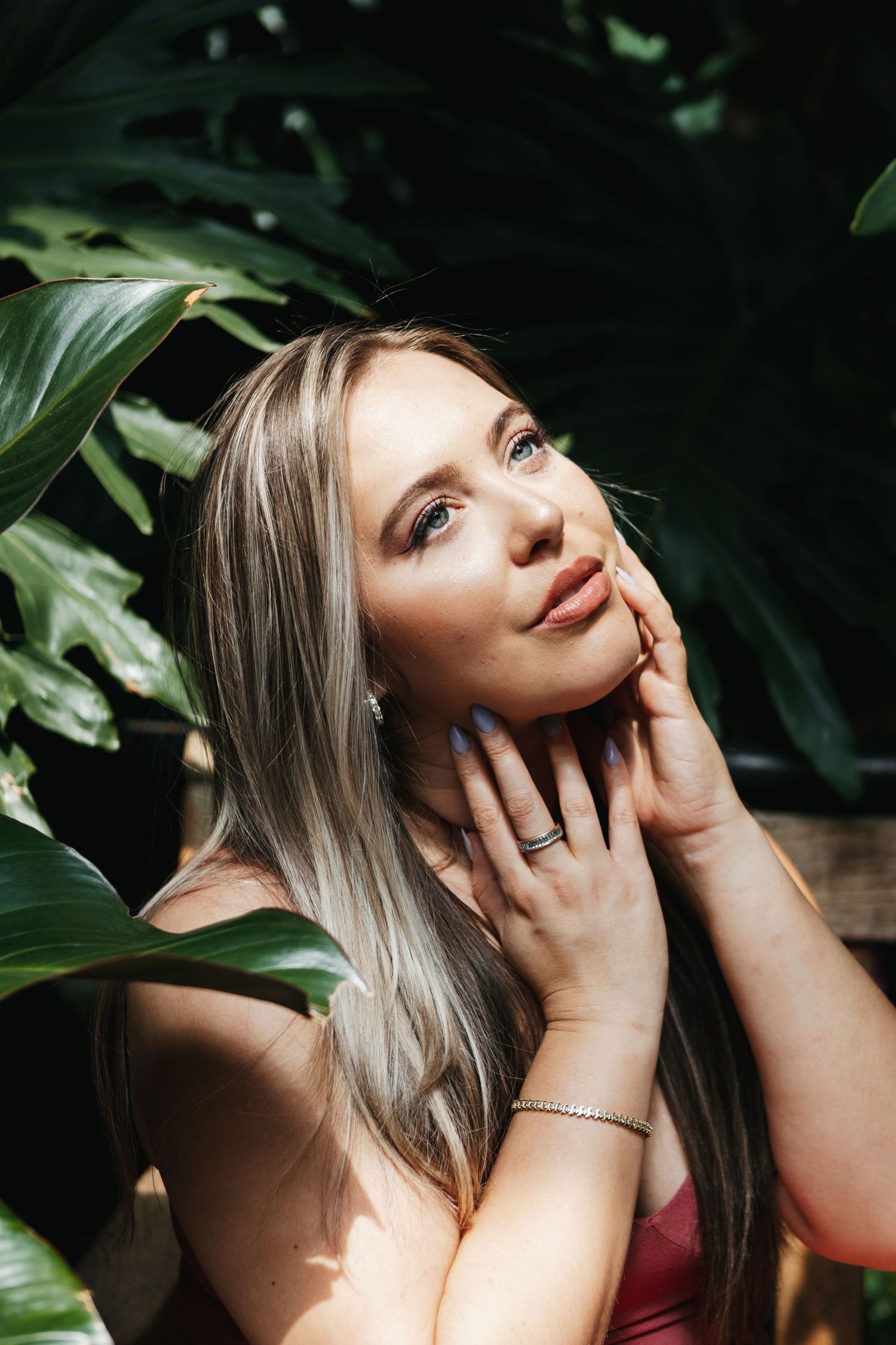 A portrait photoshoot in a botanical setting with lush green leaves framing the subject in natural light.