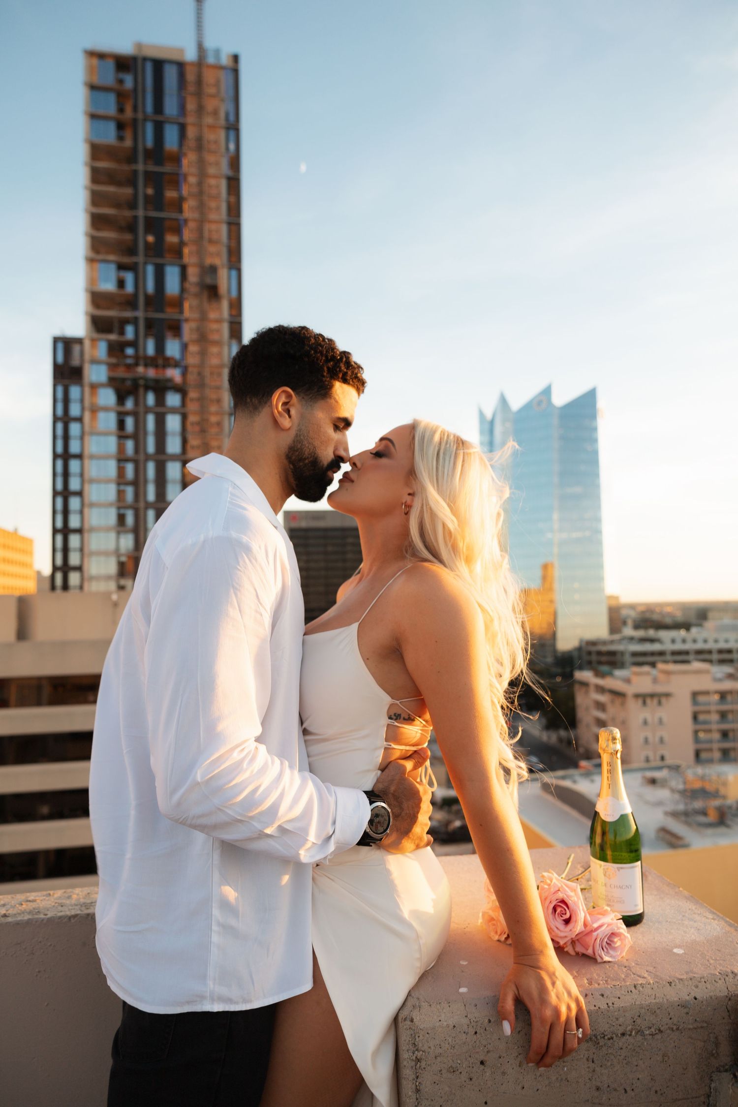 Romantic couple sharing intimate moments at sunset on an urban rooftop with city buildings in the background.