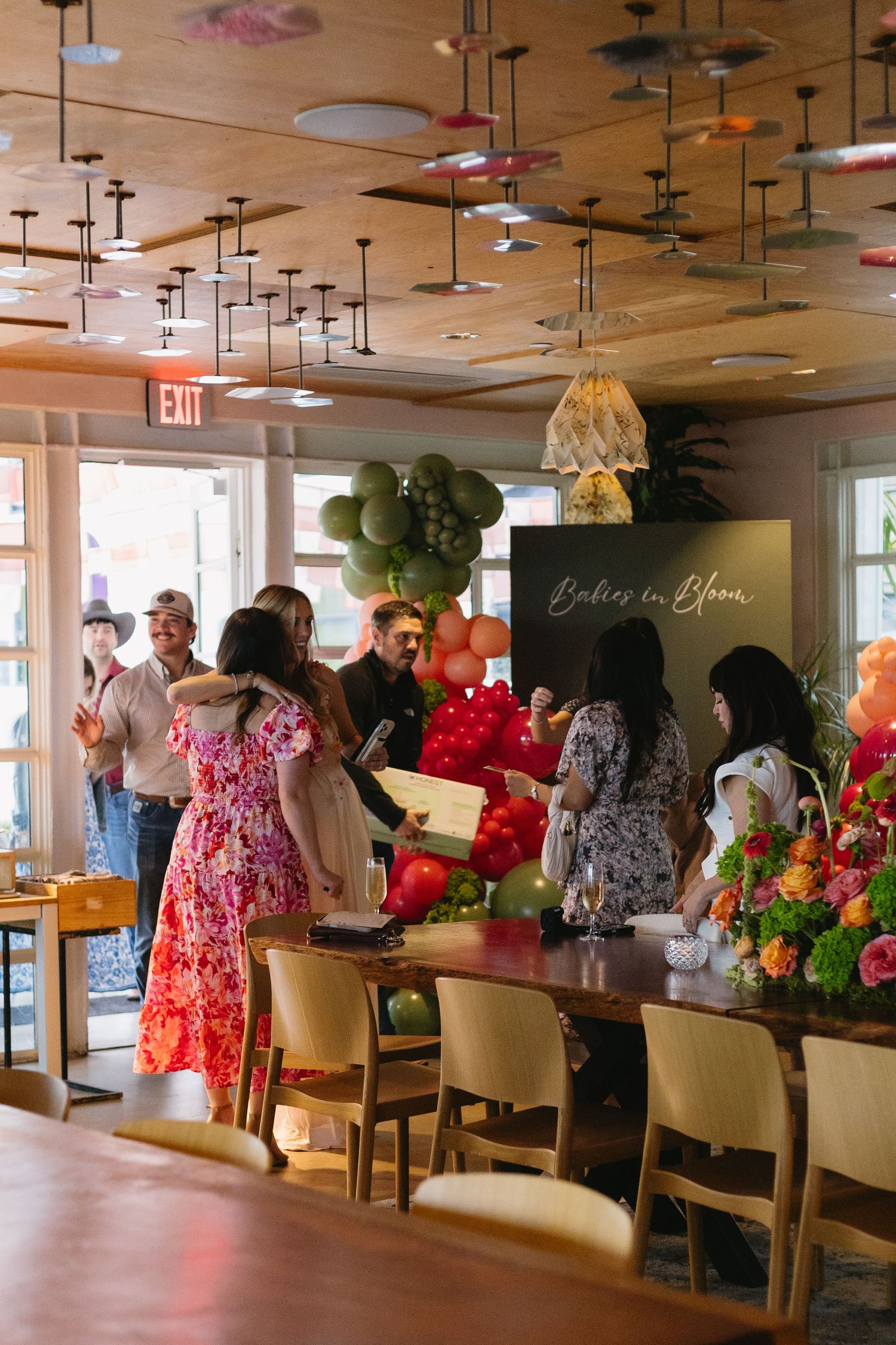 Guests gather at a Babies in Bloom baby shower event with festive balloon decorations in a restaurant.