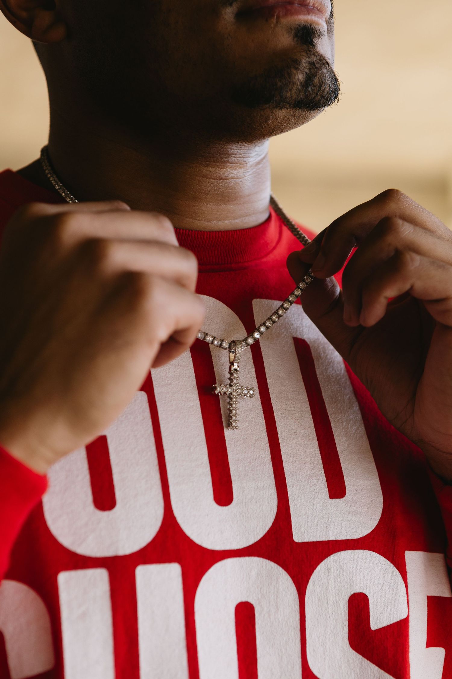 Man in red God Chose tee adjusting diamond cross necklace, close-up portrait shot.
