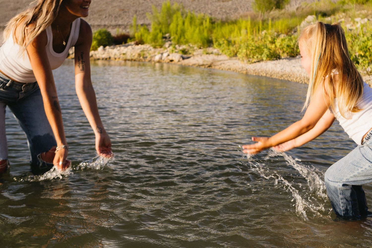 Two women splashing water in a shallow river on a sunny day outdoors.