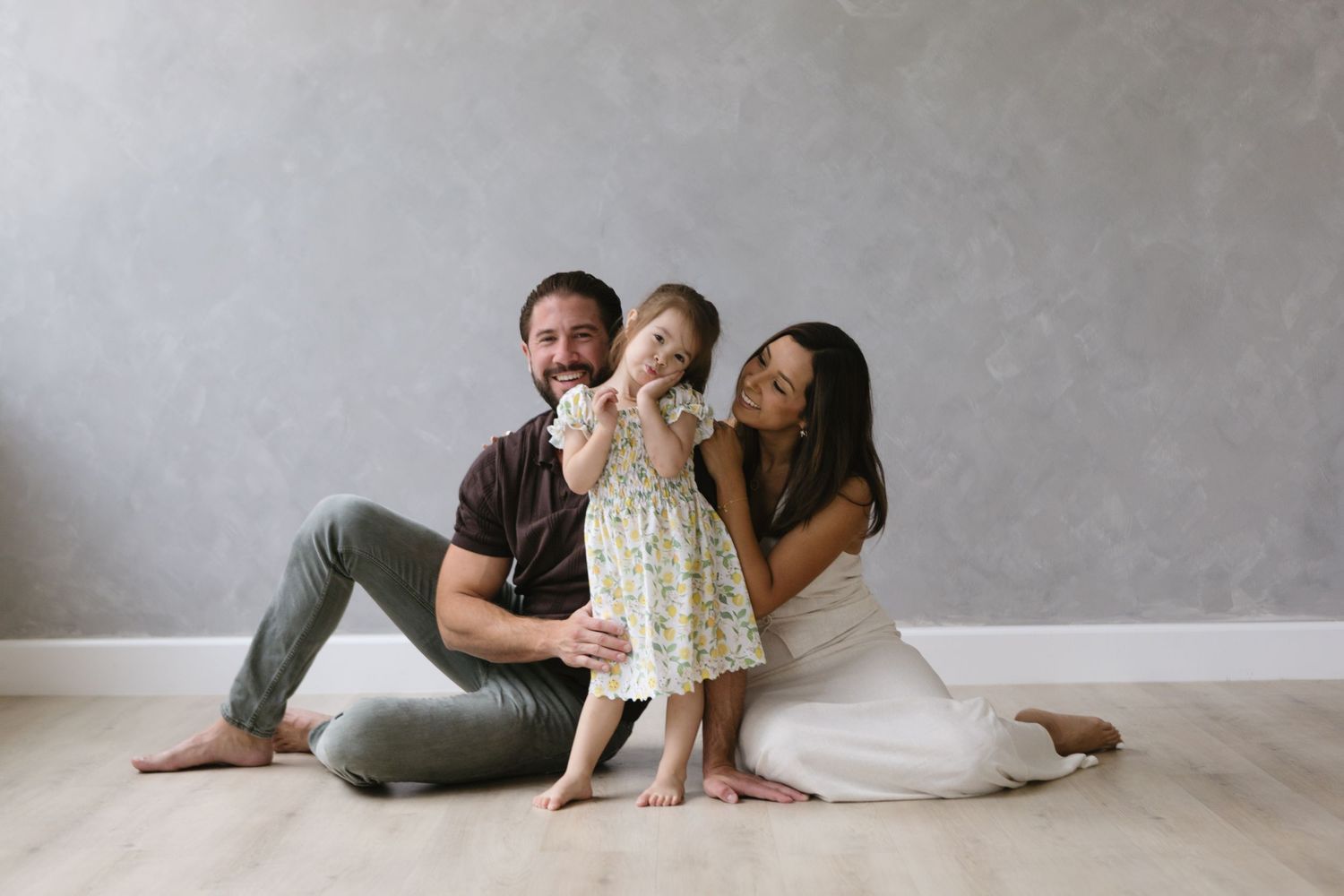 An intimate family portrait session with soft lighting against a gray wall background.