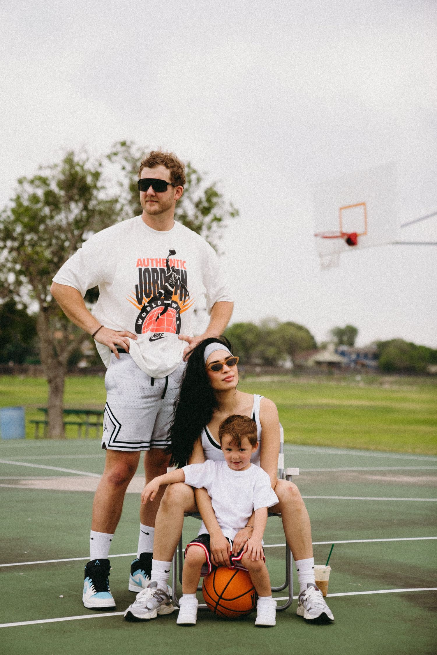 Family of three posing on basketball court with ball, wearing matching white athletic outfits.