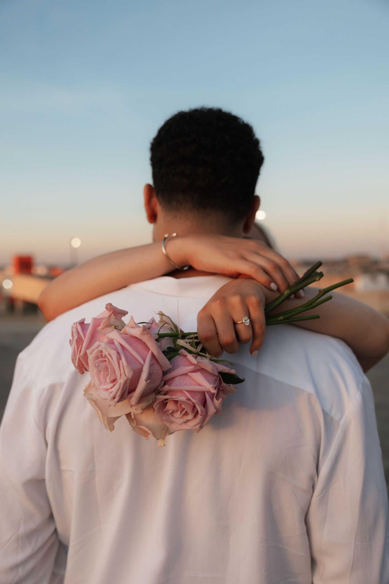 Pink roses rest against a white shirt during a sunset rooftop photoshoot.