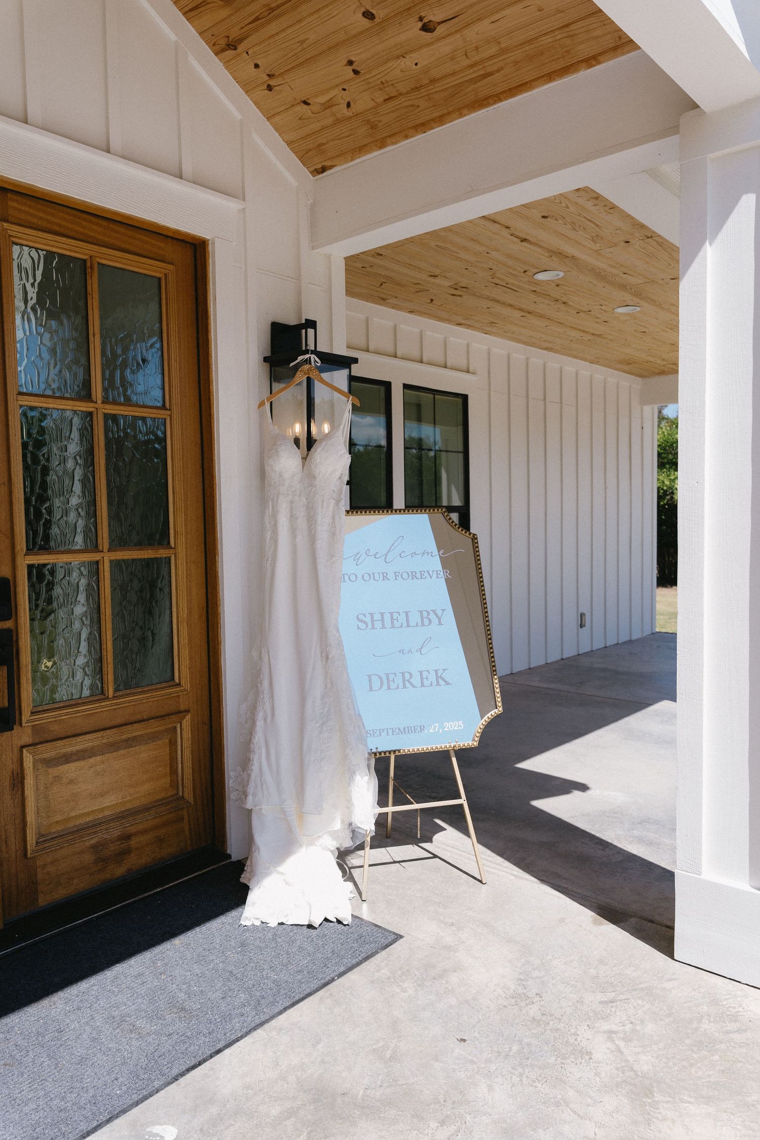 Wedding dress displayed outside a rustic venue with a welcome sign for Shelby and Derek's wedding ceremony.