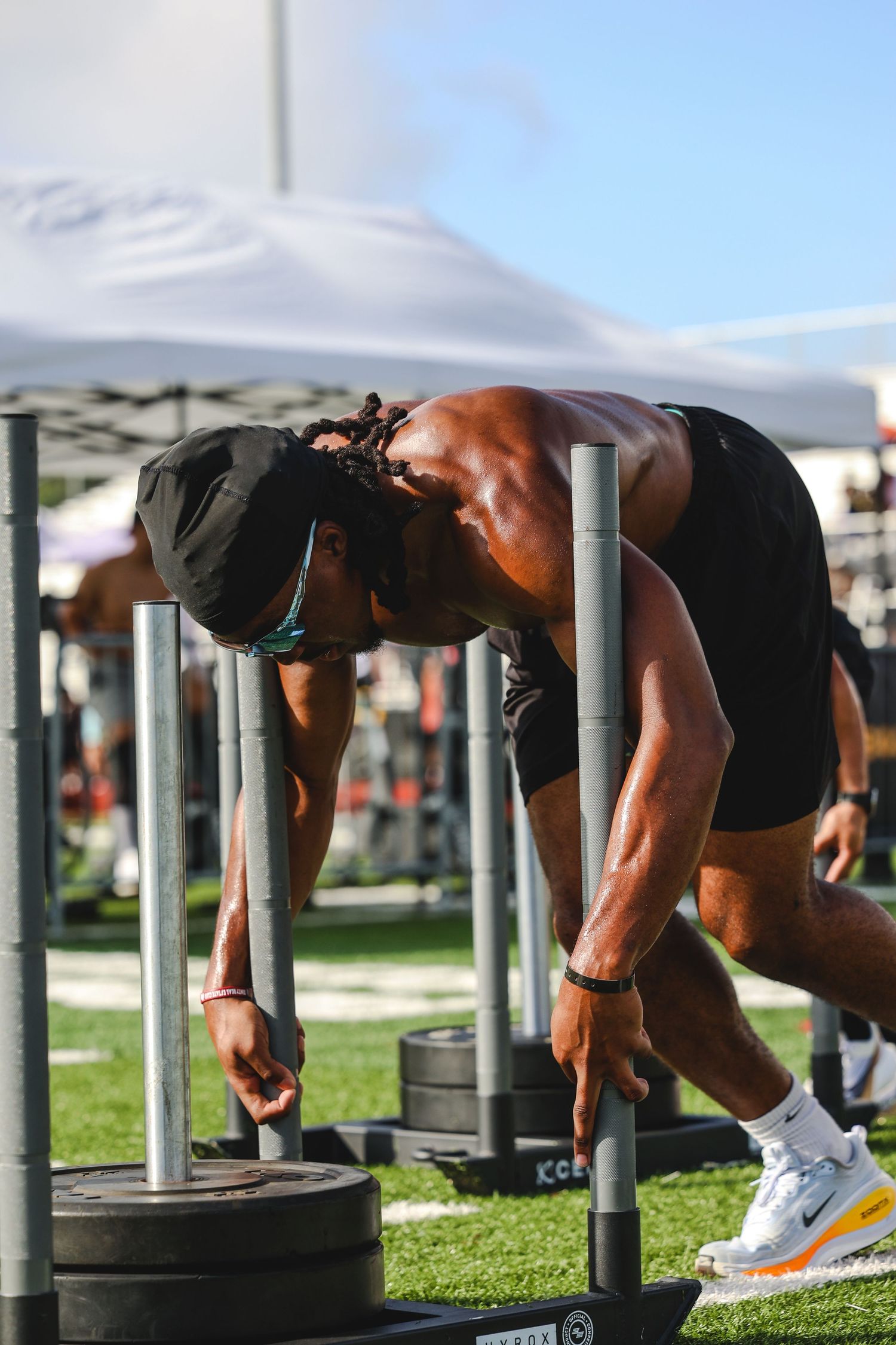 Muscular athlete lifting heavy barbell weights outdoors at a fitness competition on a green turf field.