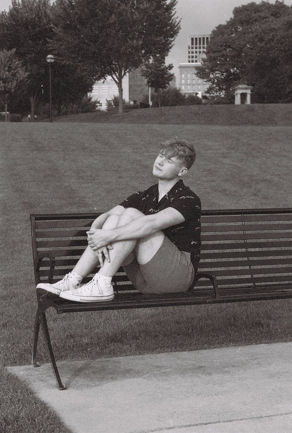 A black and white photo of a young man sitting on a park bench.