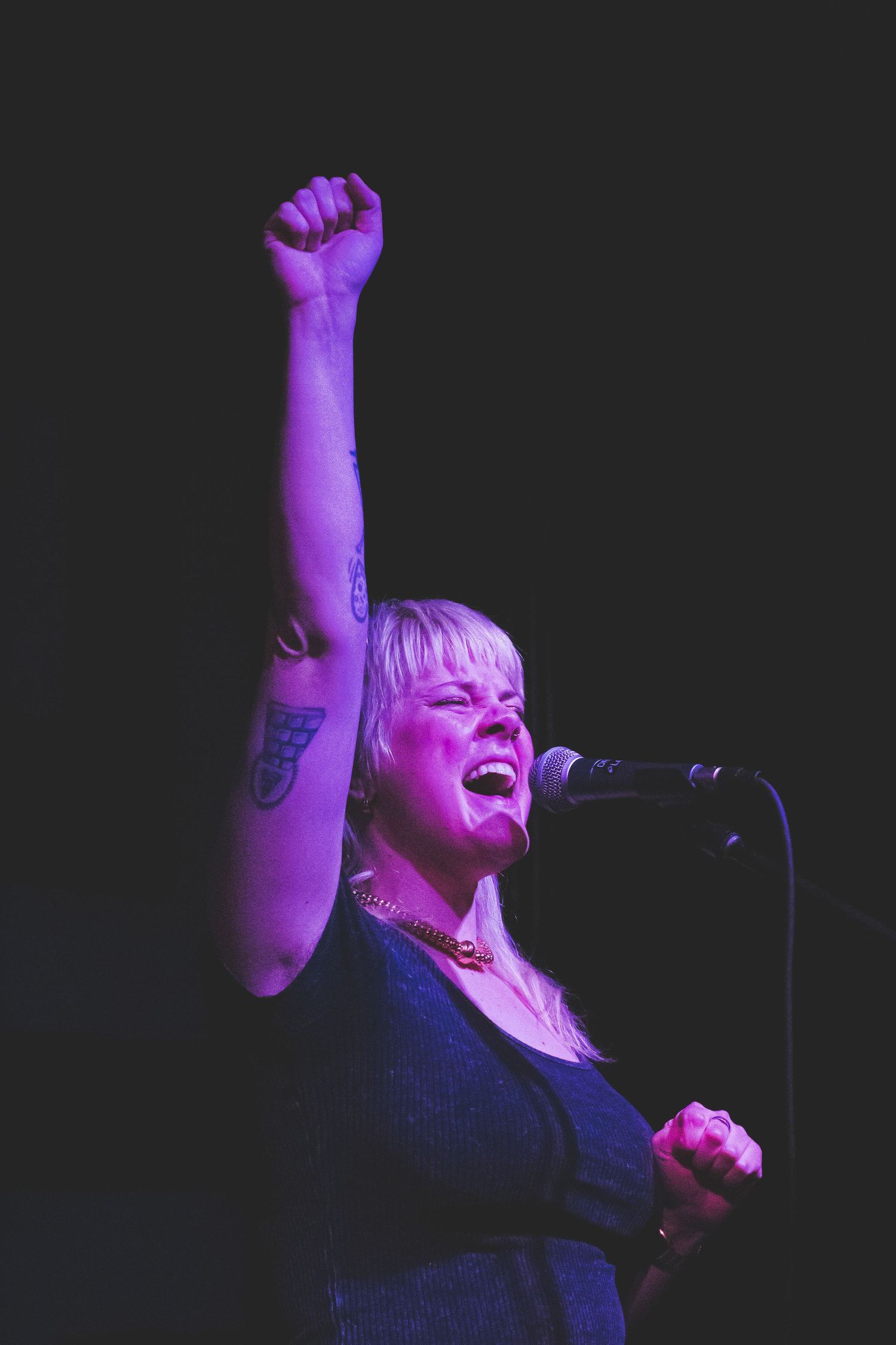 A woman singing into a microphone holding her fist into the air
