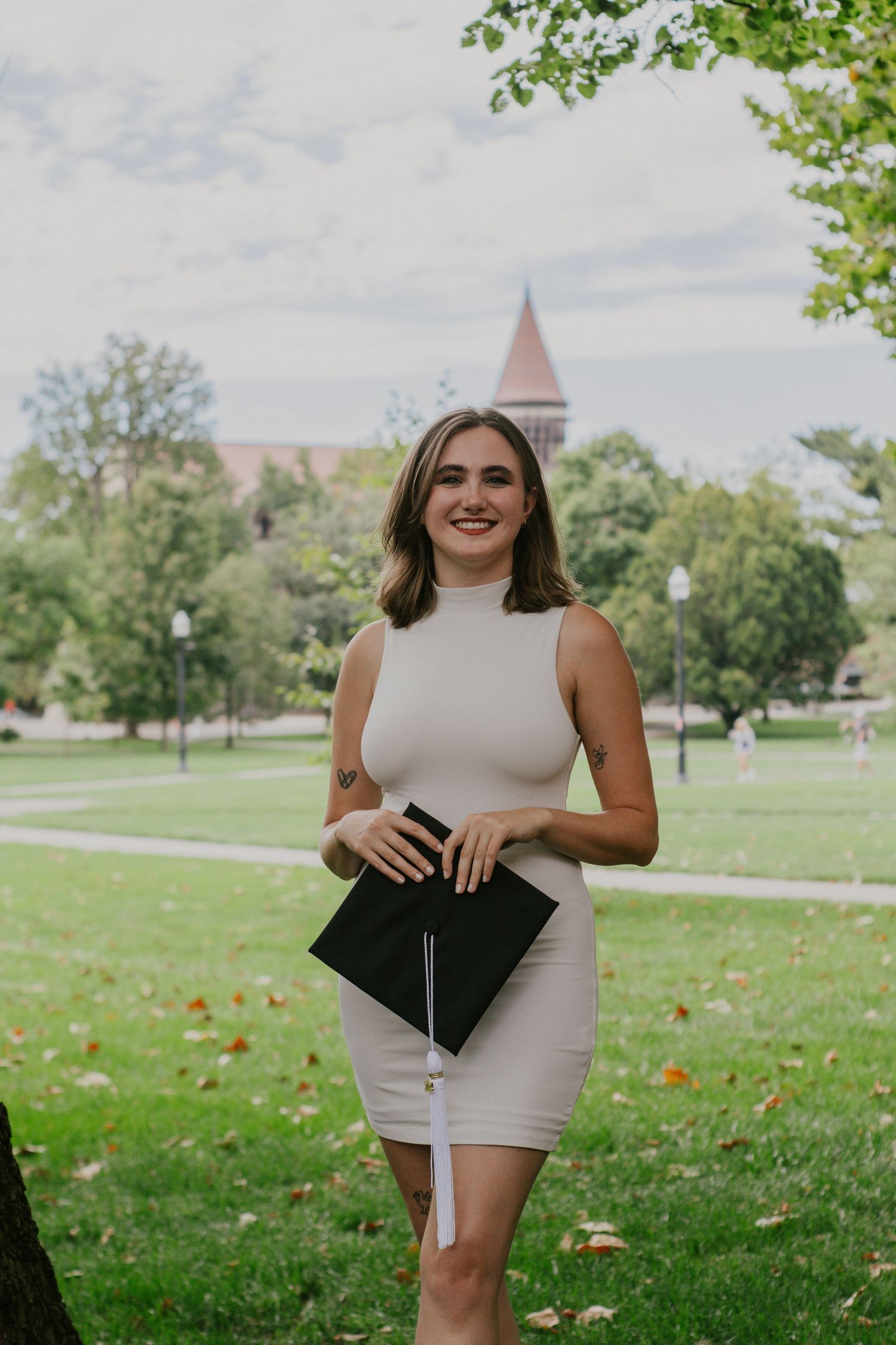 A woman standing with a graduation cap in front of grassy landscape.