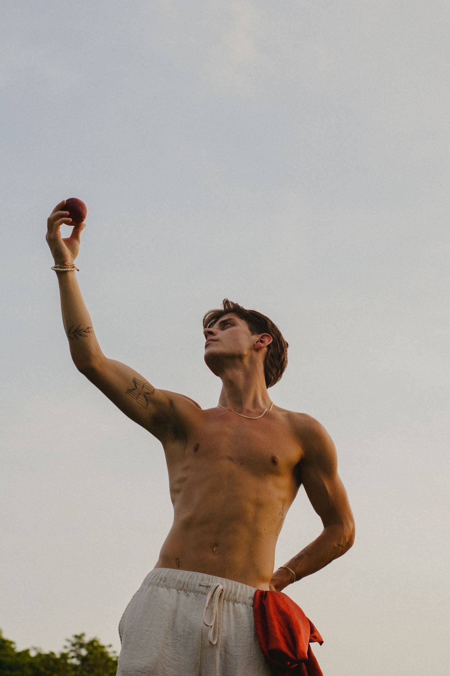 A man holding a peach in front of an overcast sky.