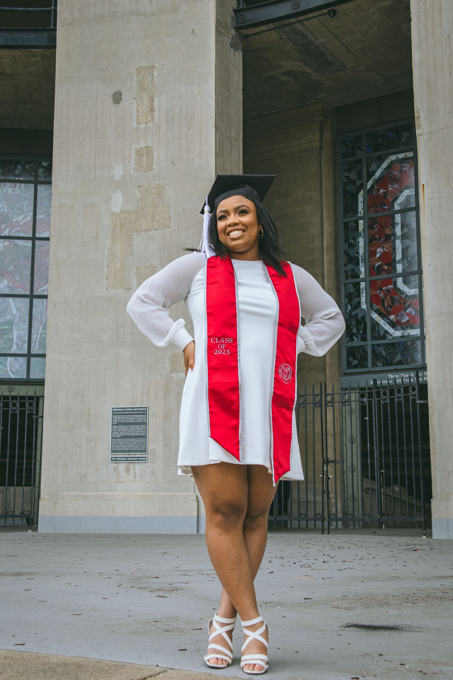 A woman in a white dress and graduation cap standing proudly in front of Ohio Stadium