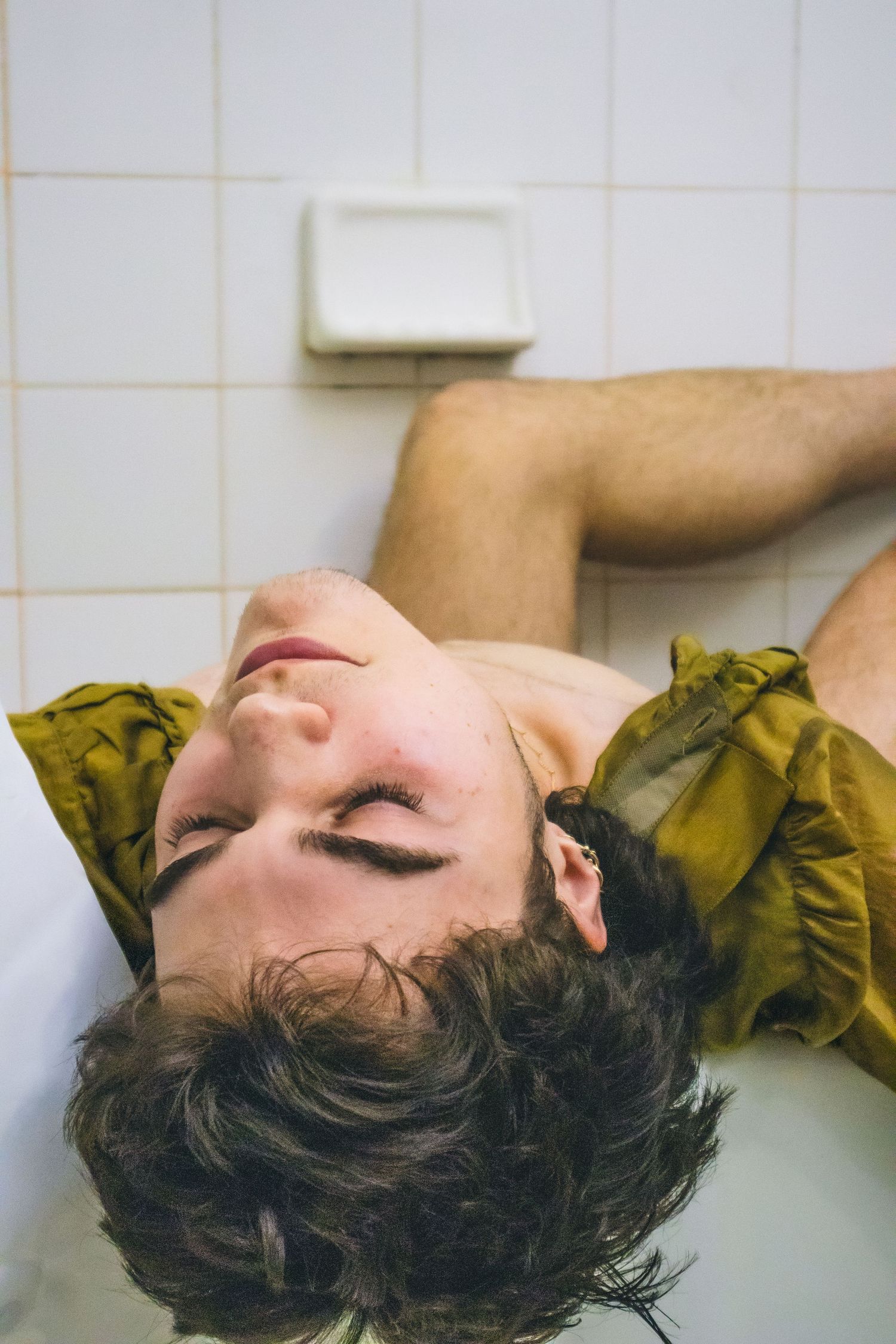 A man laying on his back on the edge of a bathtub.