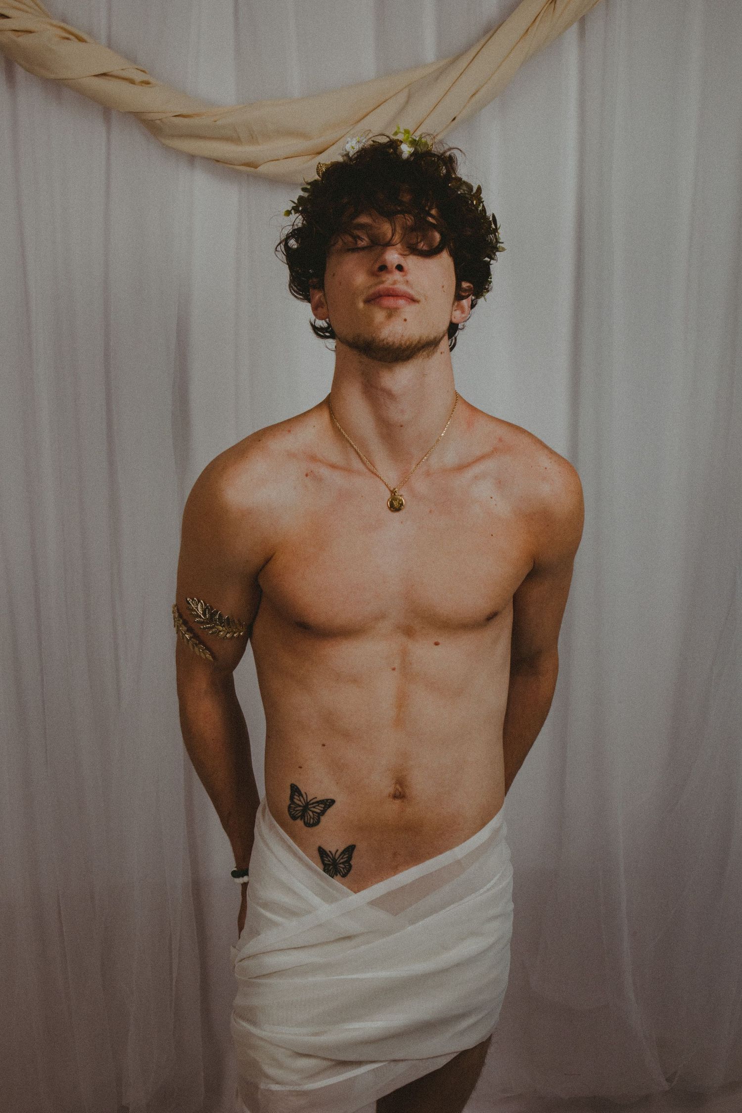A photo of a man standing in front of a white curtain backdrop with a white fabric across his waist
