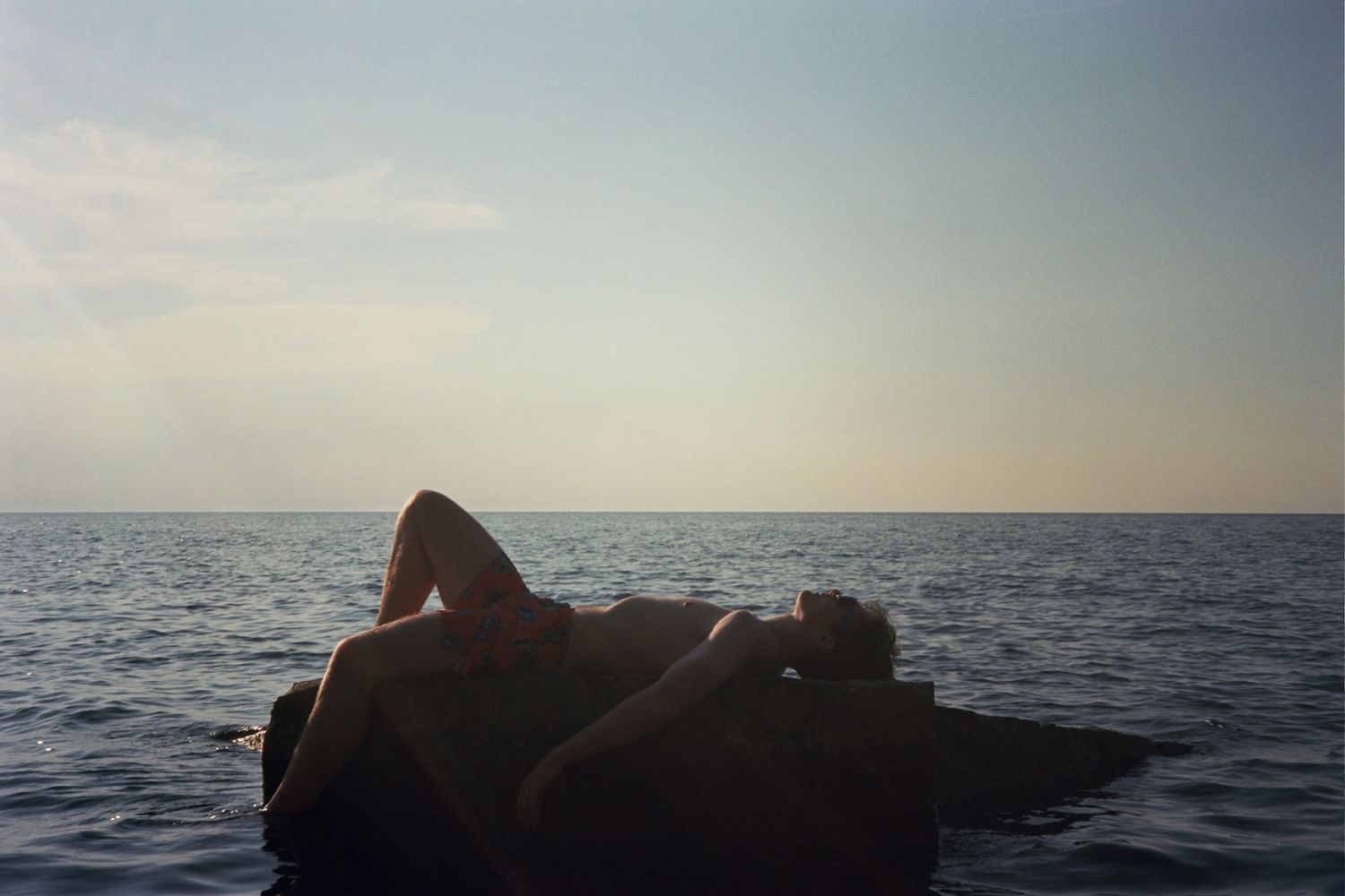 A man laying on a rock in the middle of the water