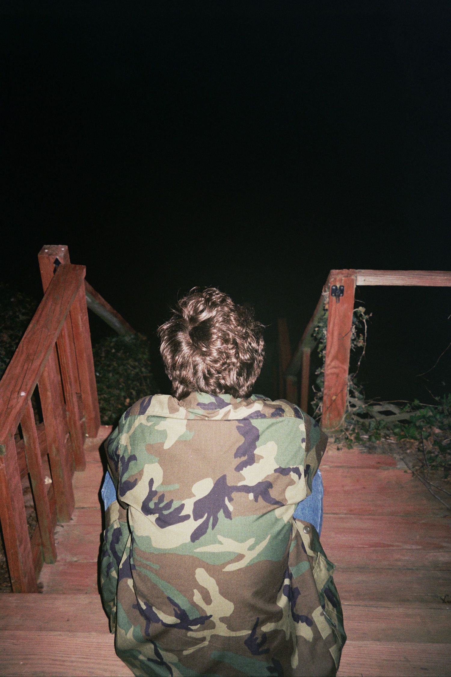 A man sitting on a wooden deck looking out into the darkness