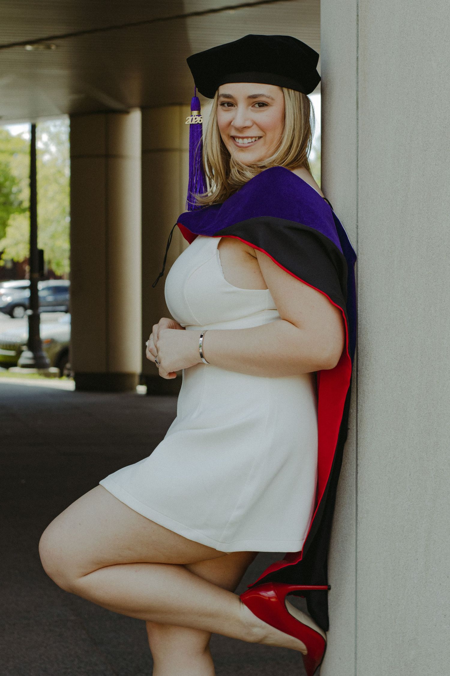 A law school graduate leaning against a concrete pillar.