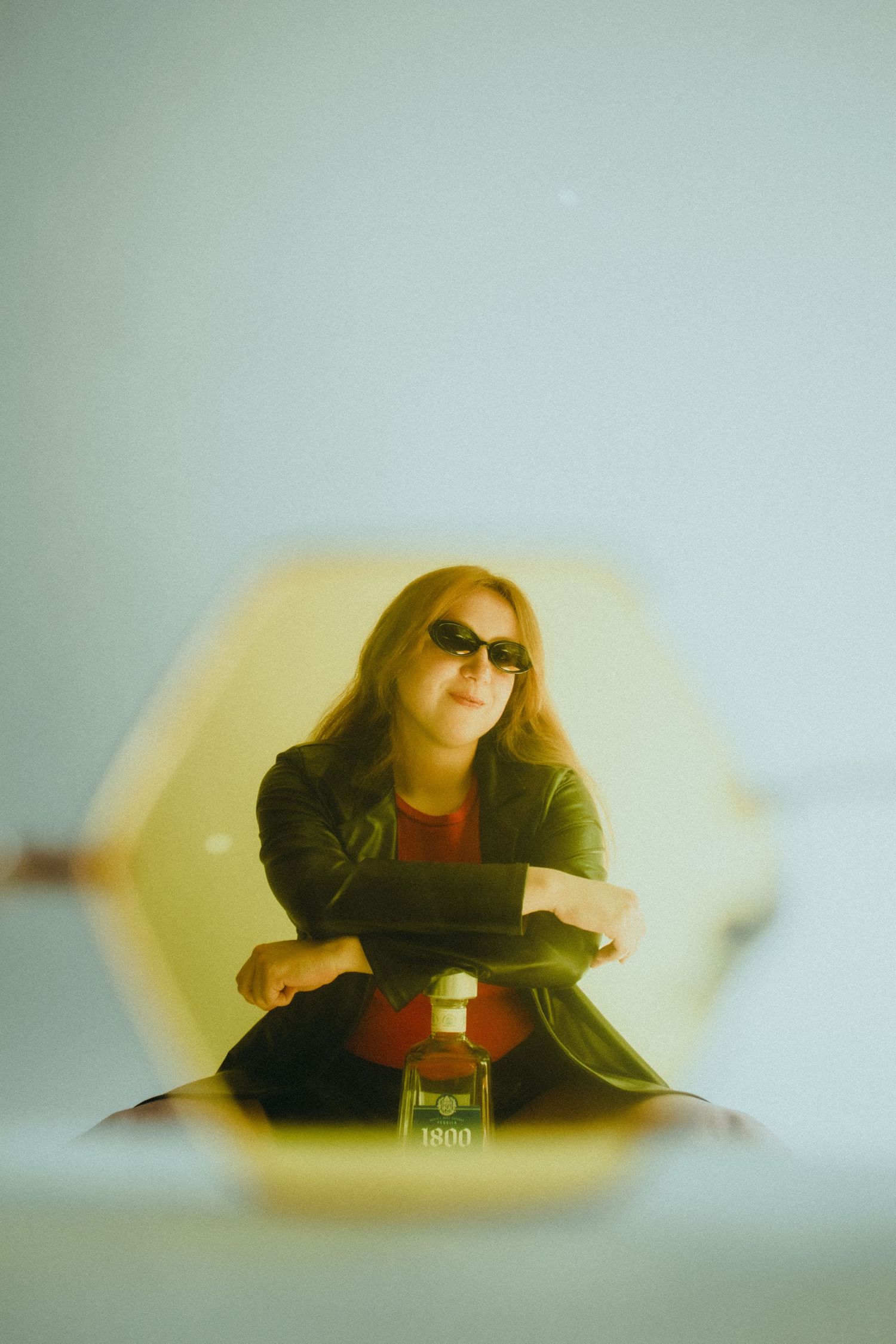 A woman sitting on the floor in front of a white background with a bottle of tequila in front of her.