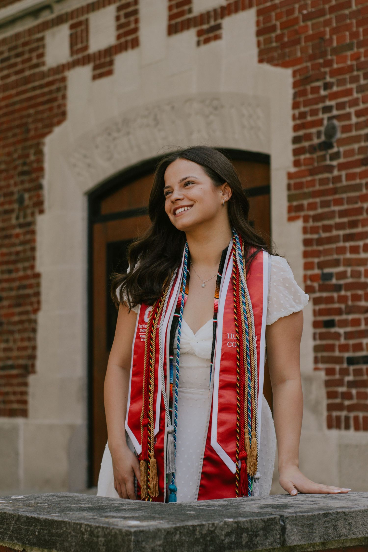 A woman wearing multiple cords and stoles standing in front of a brick building