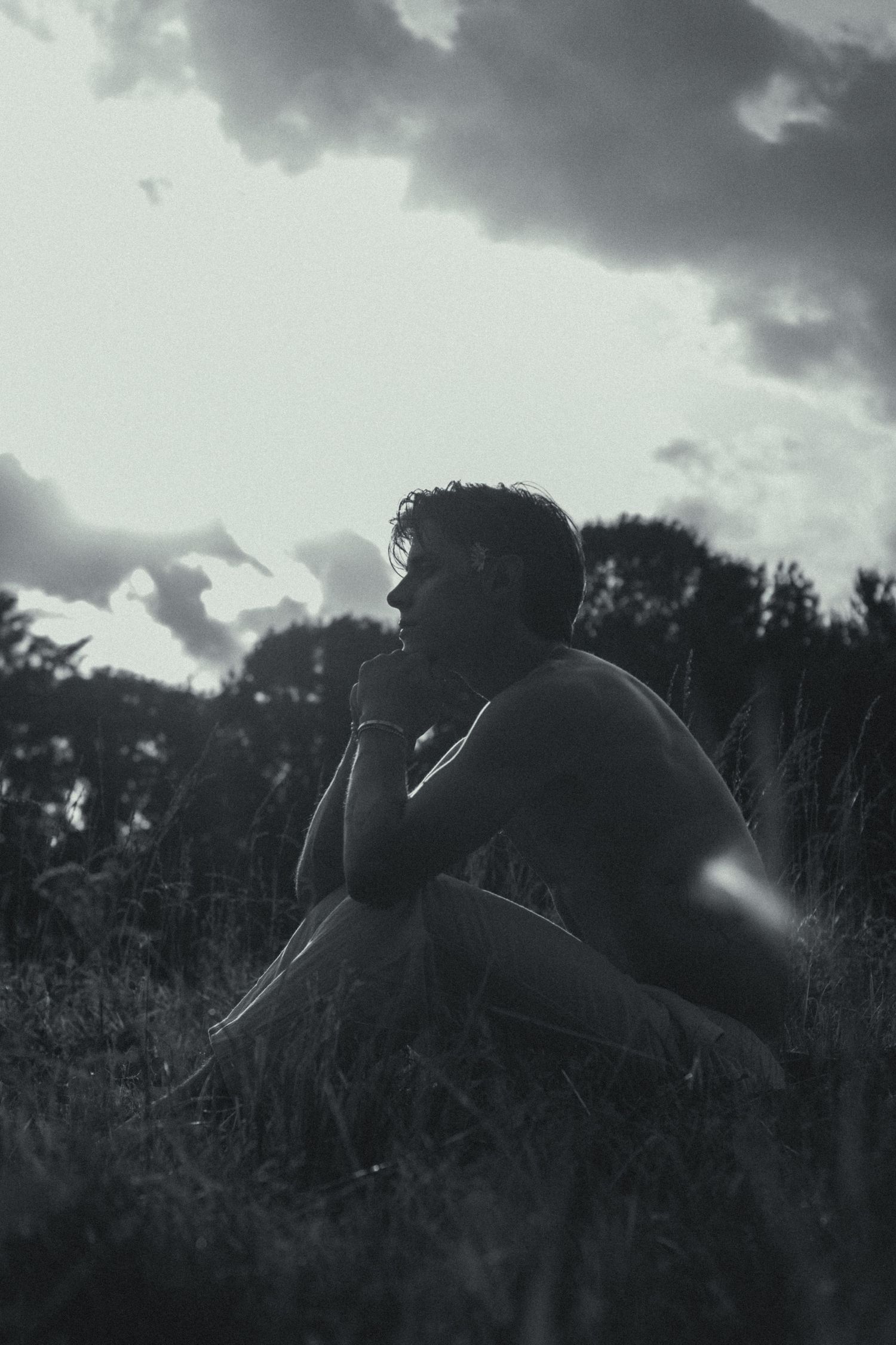 A man sitting in a grassy field with his head in his hands.