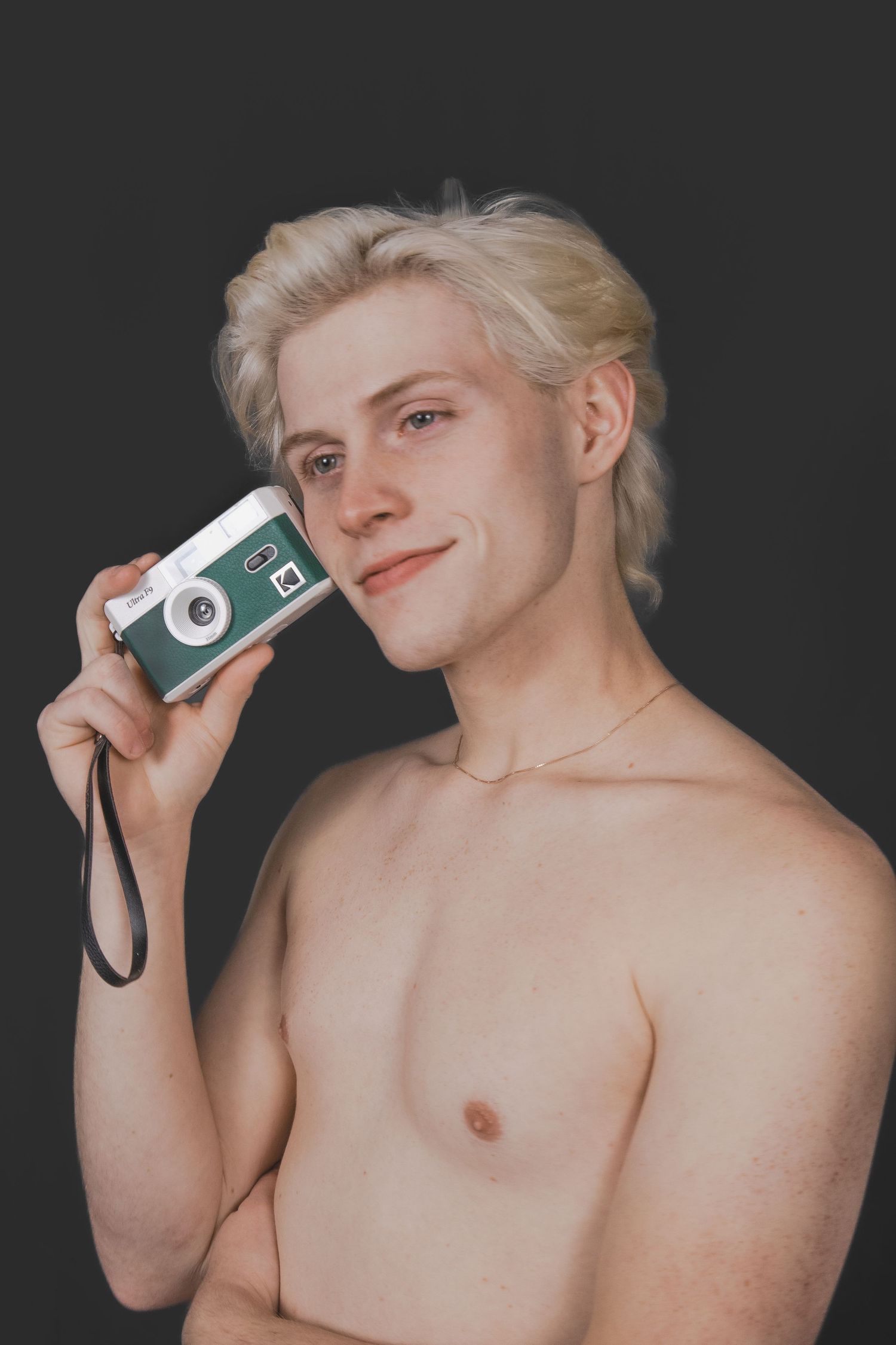 A shirtless man holding a green and white camera to his head.