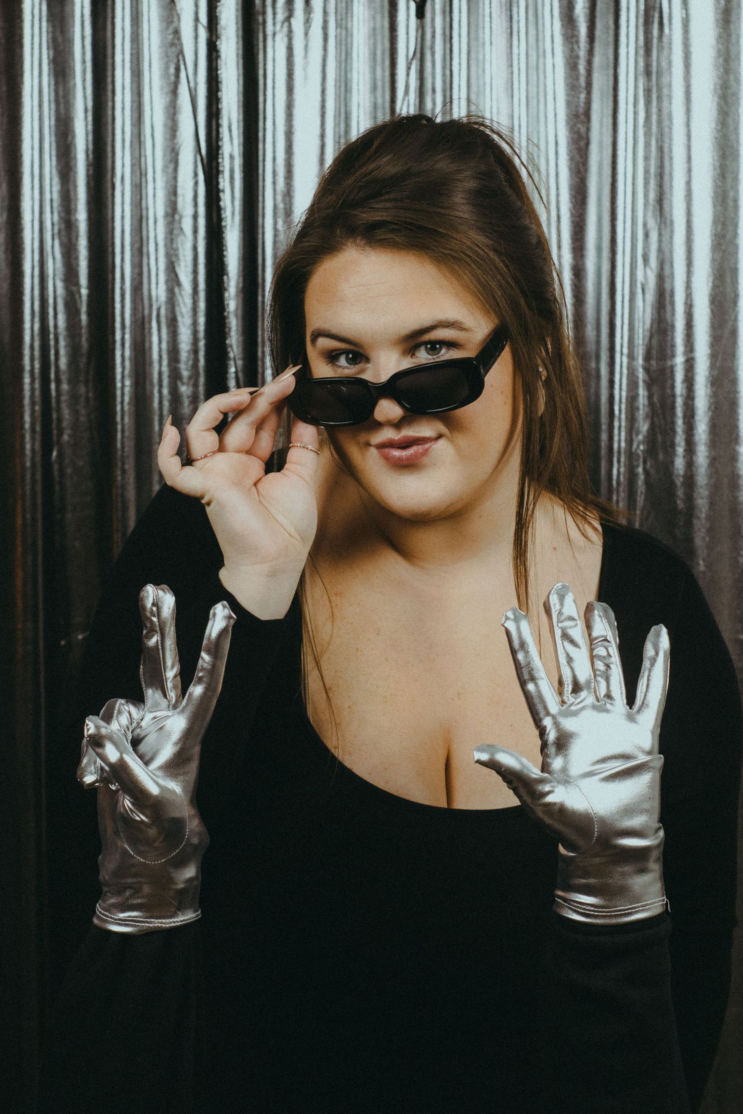 A photo of a woman standing in front of a silver, shimmering backdrop.