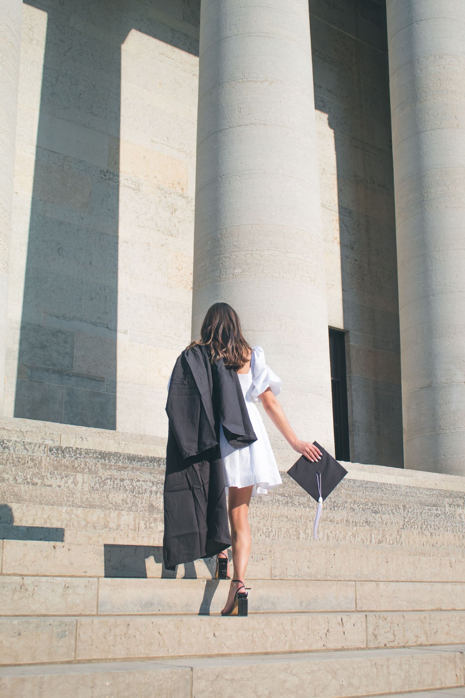 A woman in her cap and gown walking up stone stairs