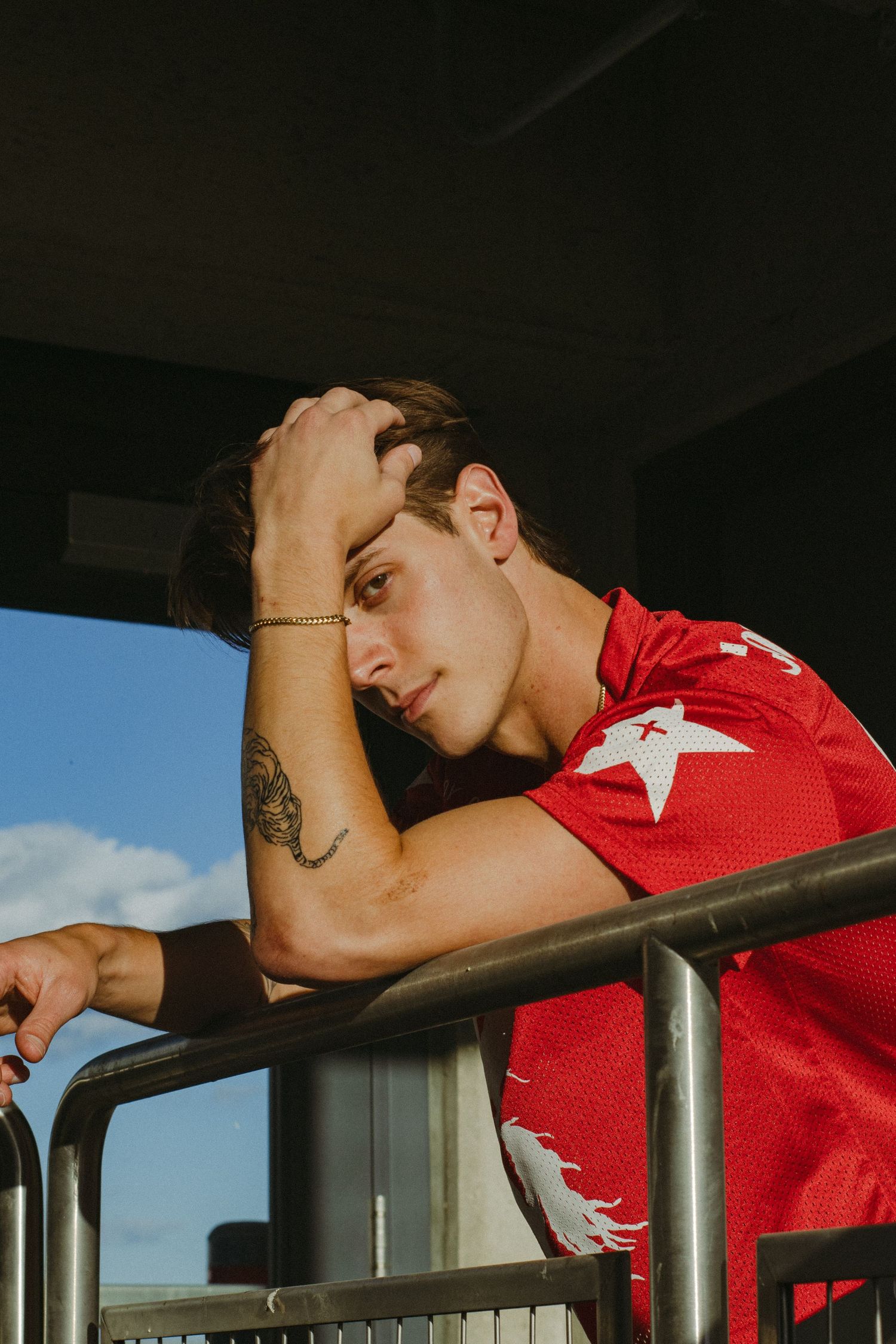 A man posing with his arm covering his face while leaning on a railing.