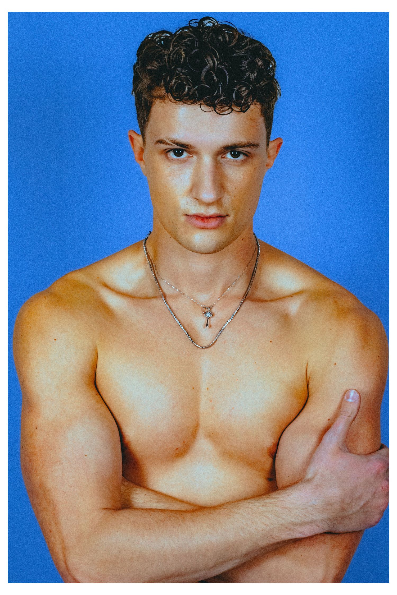 A shirtless man posing in front of a blue backdrop.