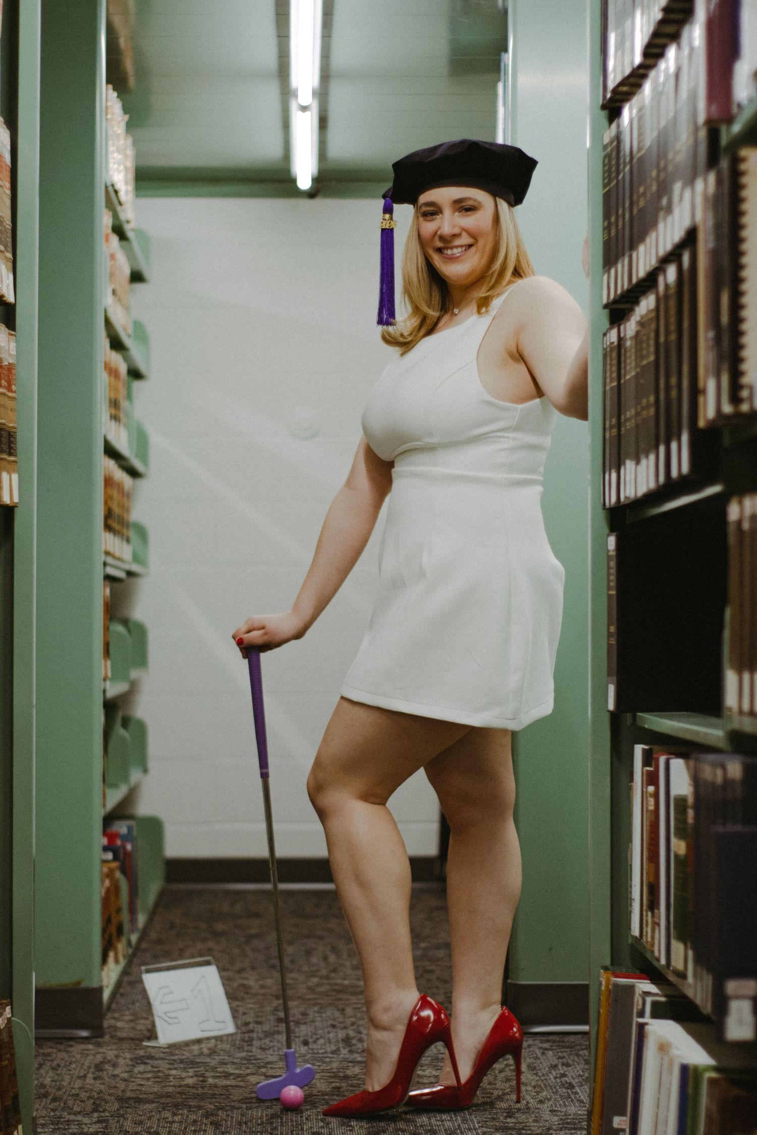 A law school graduate standing with a golf club amongst shelves of books.