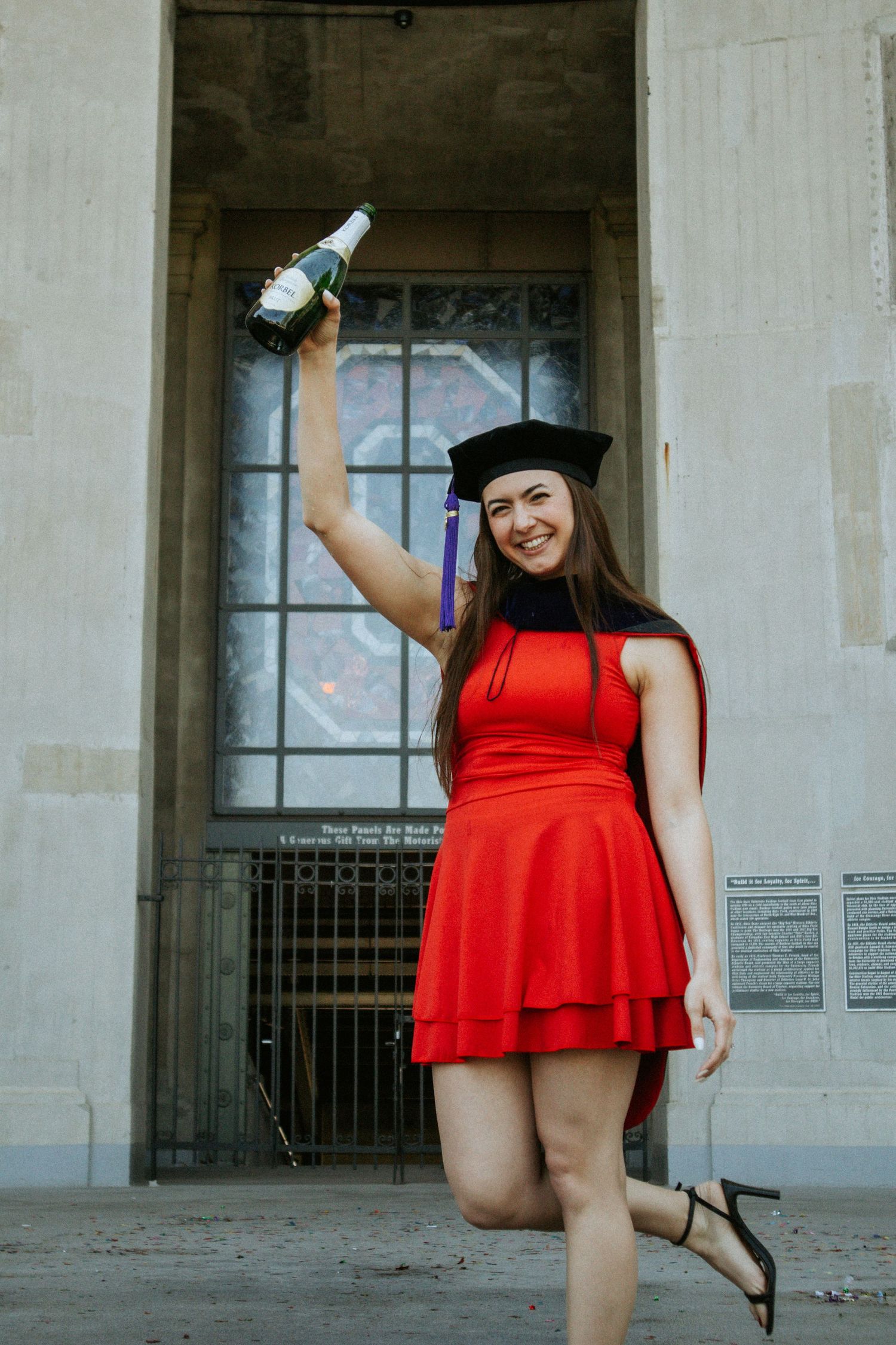 A woman holding a bottle of champagne over her head in front of a stained glass window depicting the 
